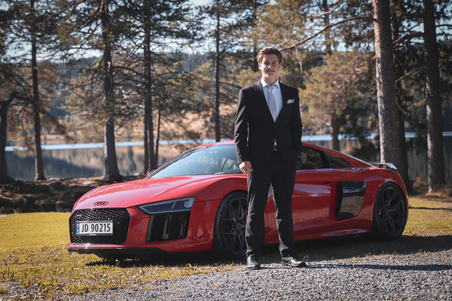 Konfirmant i svart dress fotografert med en rød Audi R8 ved Skumsjøen i Gjøvik.