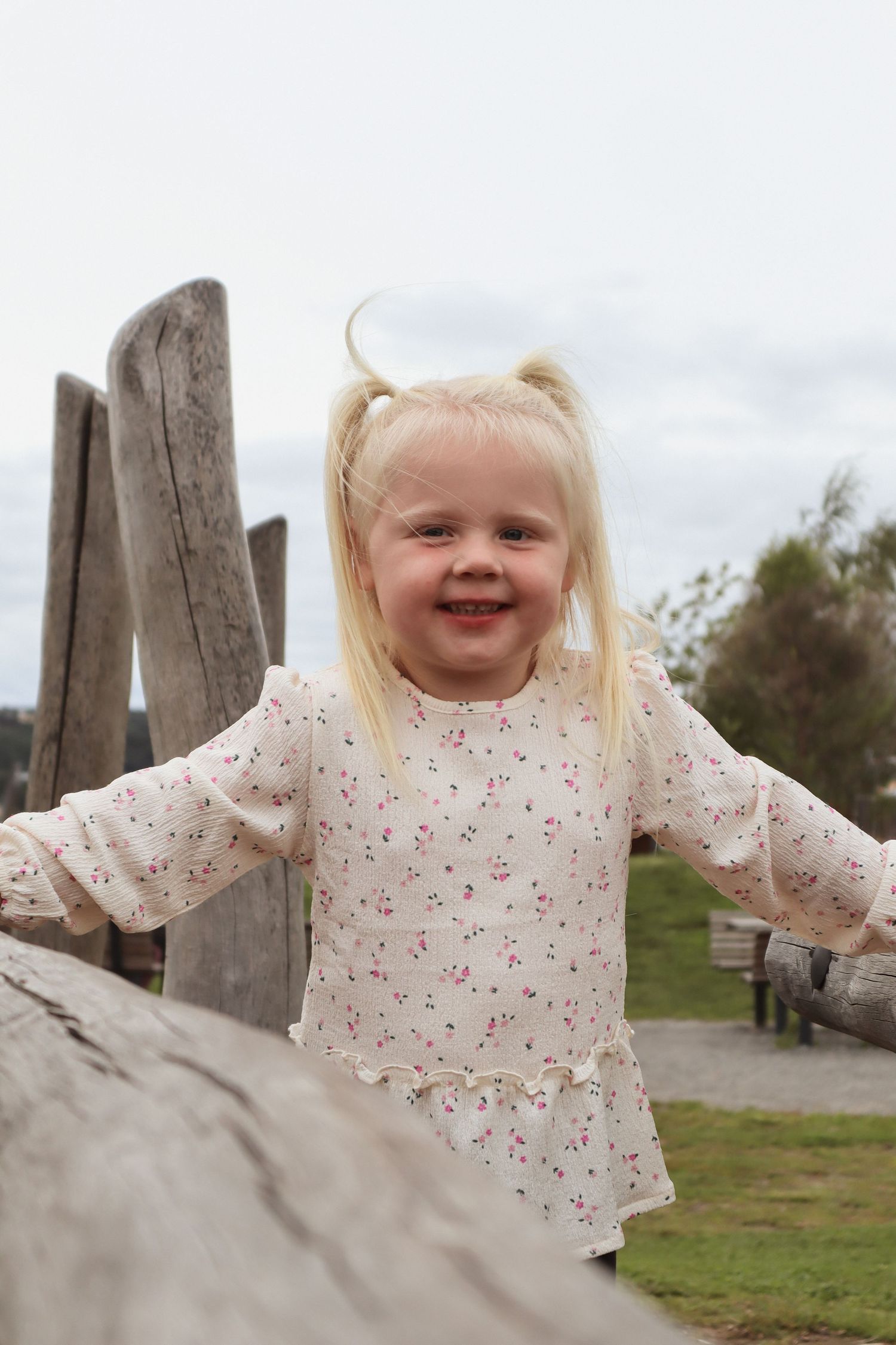 Liten jente med musefletter og blomstrete kjole lekende på lekeapparat i Mjøsparken.