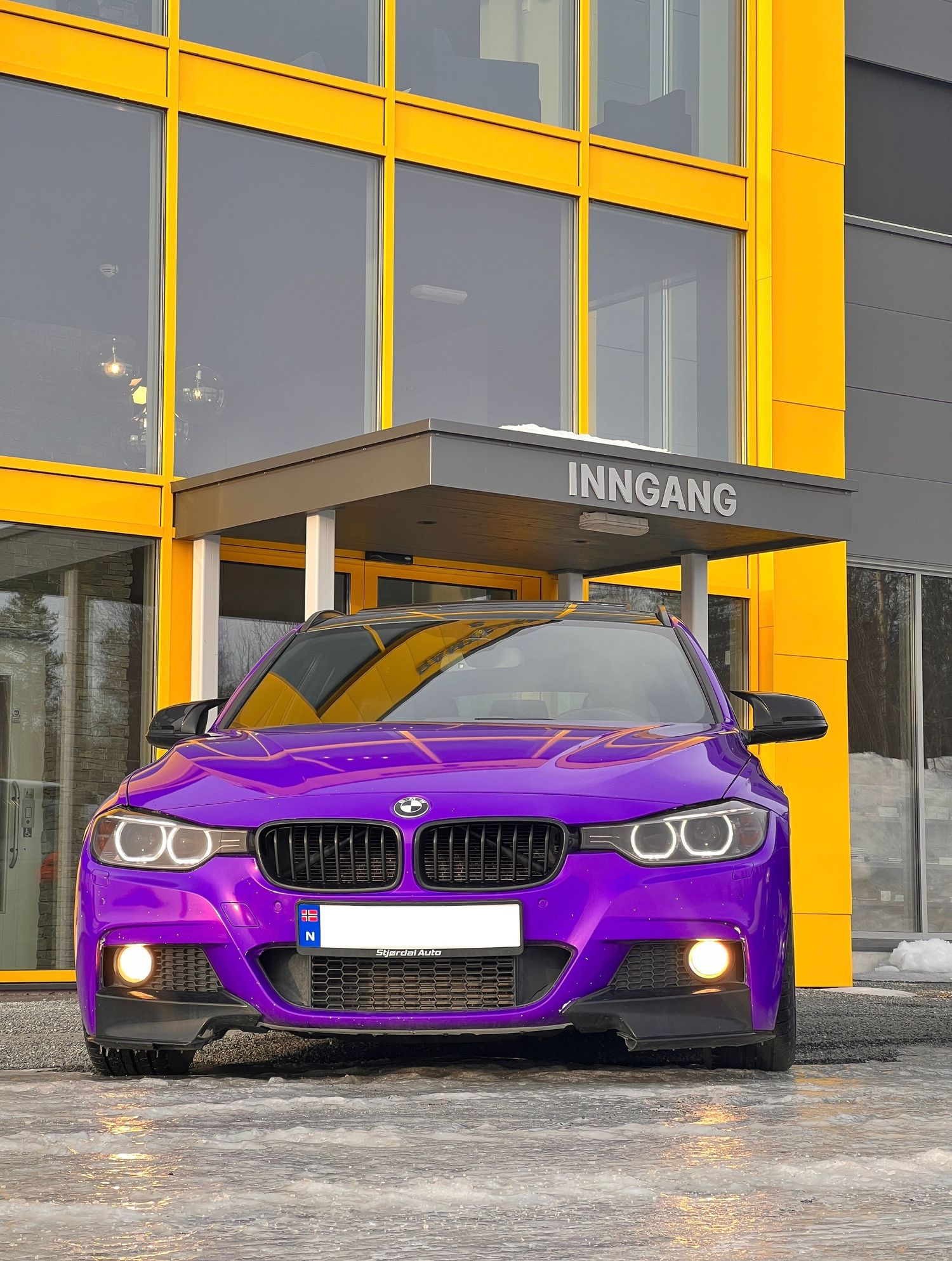 Lilla BMW fotografert foran en gul bygning med glassinngang om vinteren.