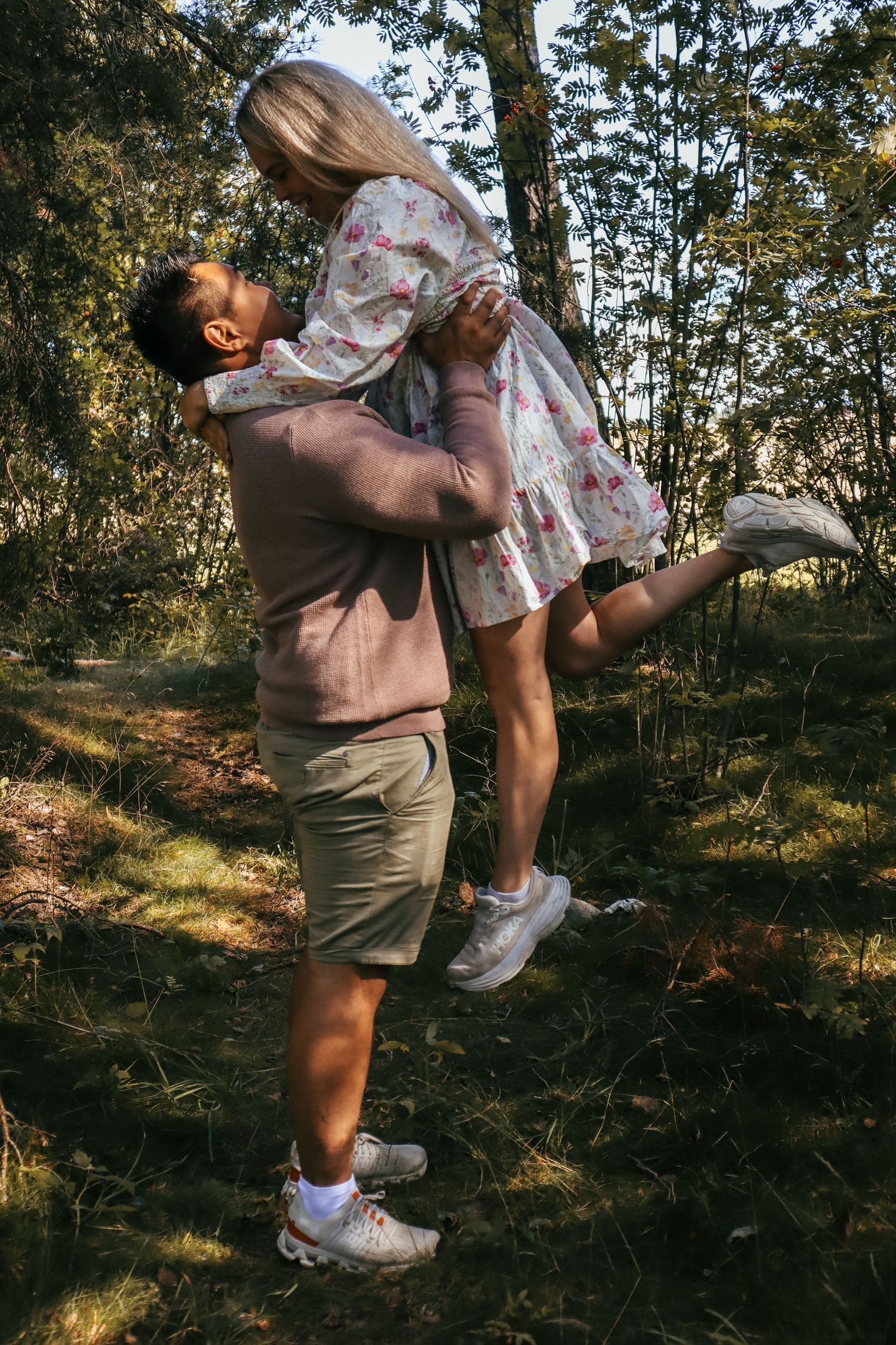Mann som løfter kvinnen under parfotografering i en solfylt skog.