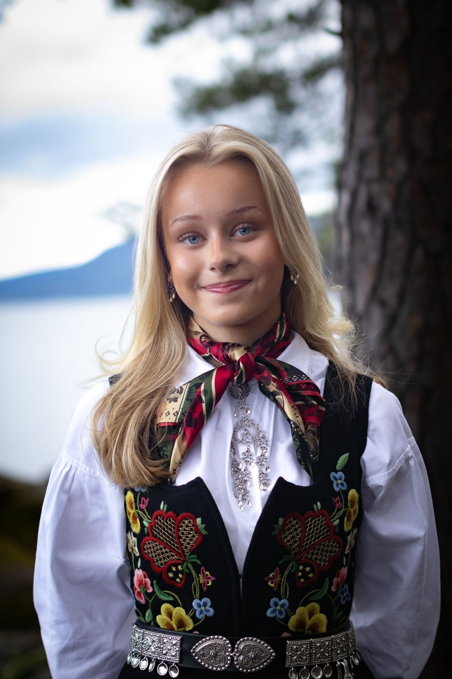 Smilende konfirmant i brodert norsk bunad fotografert utendørs.