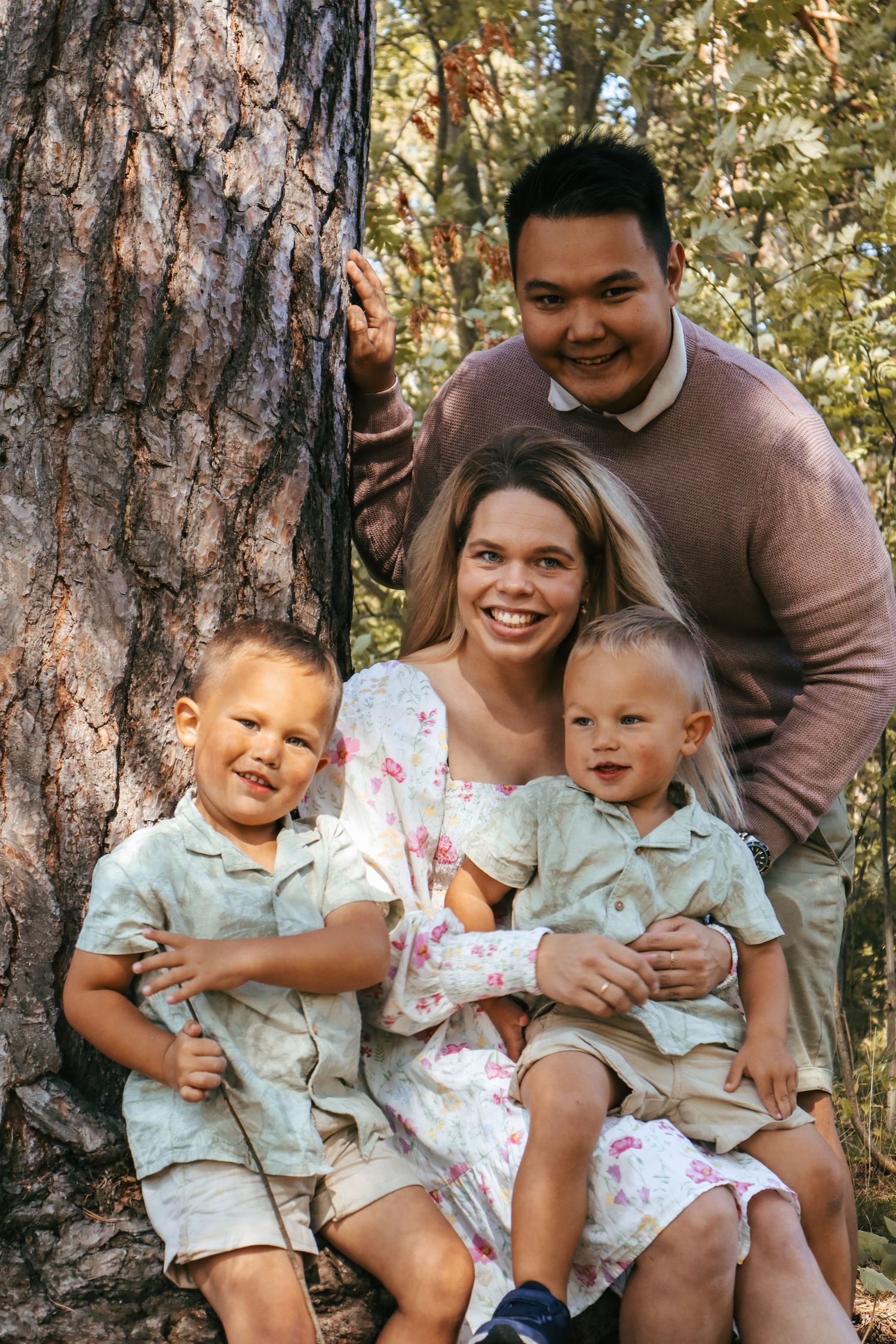 Familie på fire med to gutter fotografert ved et stort tre i skogen.