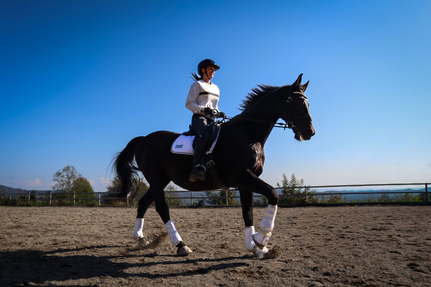 Rytter på svart hest under ridning på utendørs ridebane.
