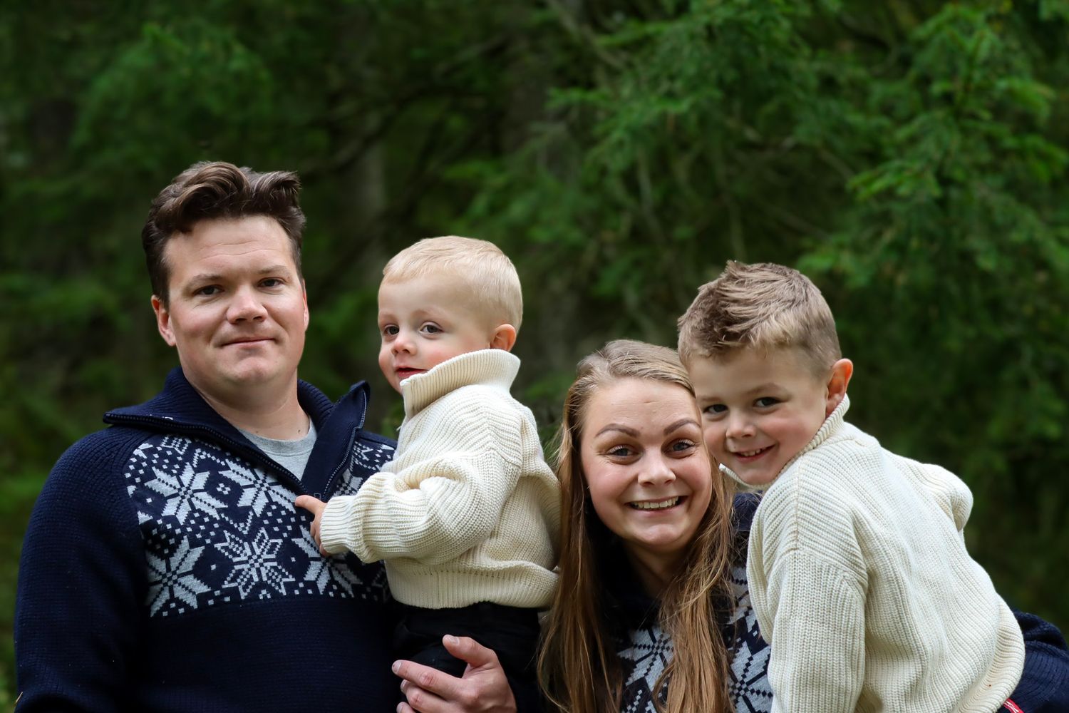 Familie på fire fotografert sammen utendørs i matchende nordiske strikkegensere.