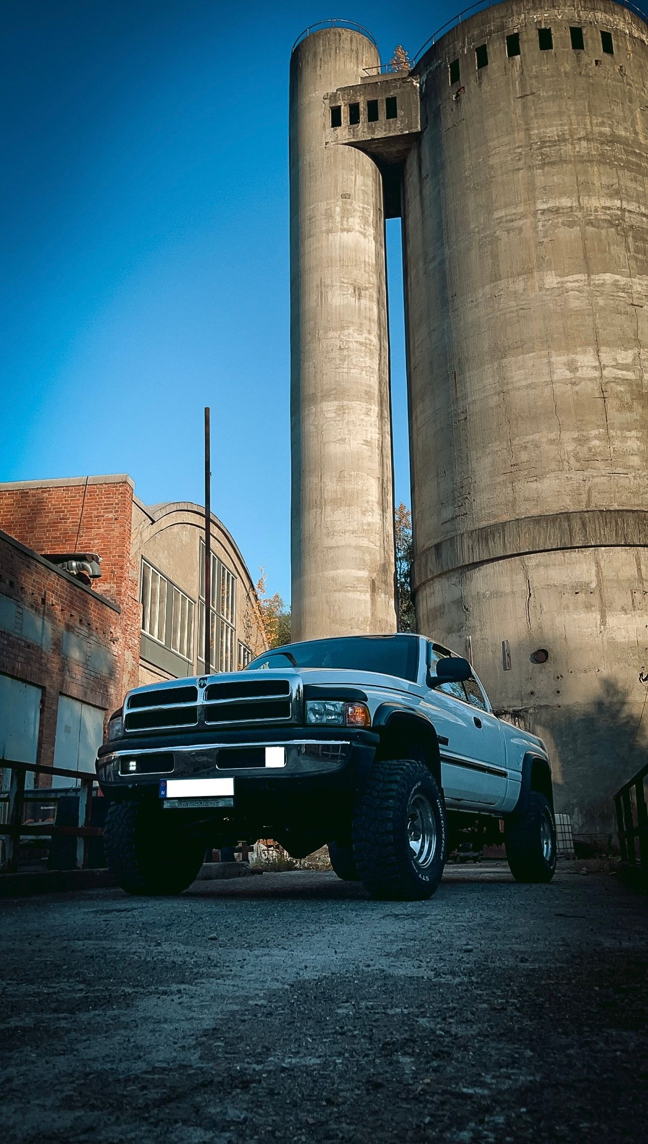 Hvit Dodge Ram pickup fotografert foran store betongsiloer under blå himmel.