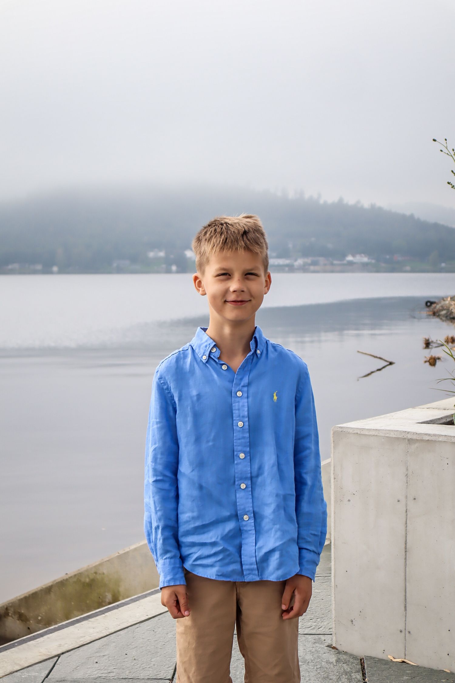 Gutt i blå linskjorte fotografert på en brygge ved tåket mjøsvann