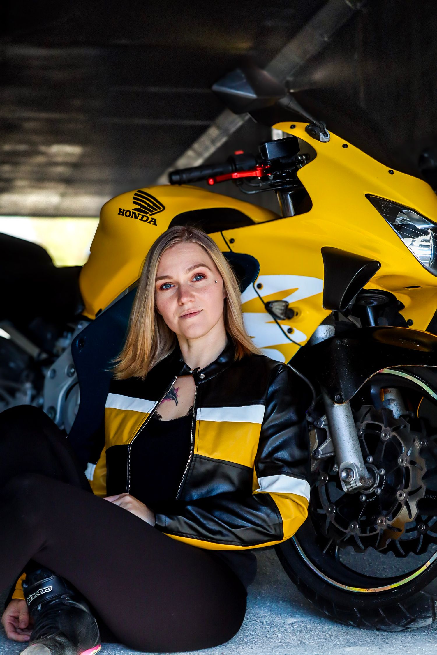 Kvinne i gul og svart skinnjakke fotografert sammen med en gul Honda motorsykkel.