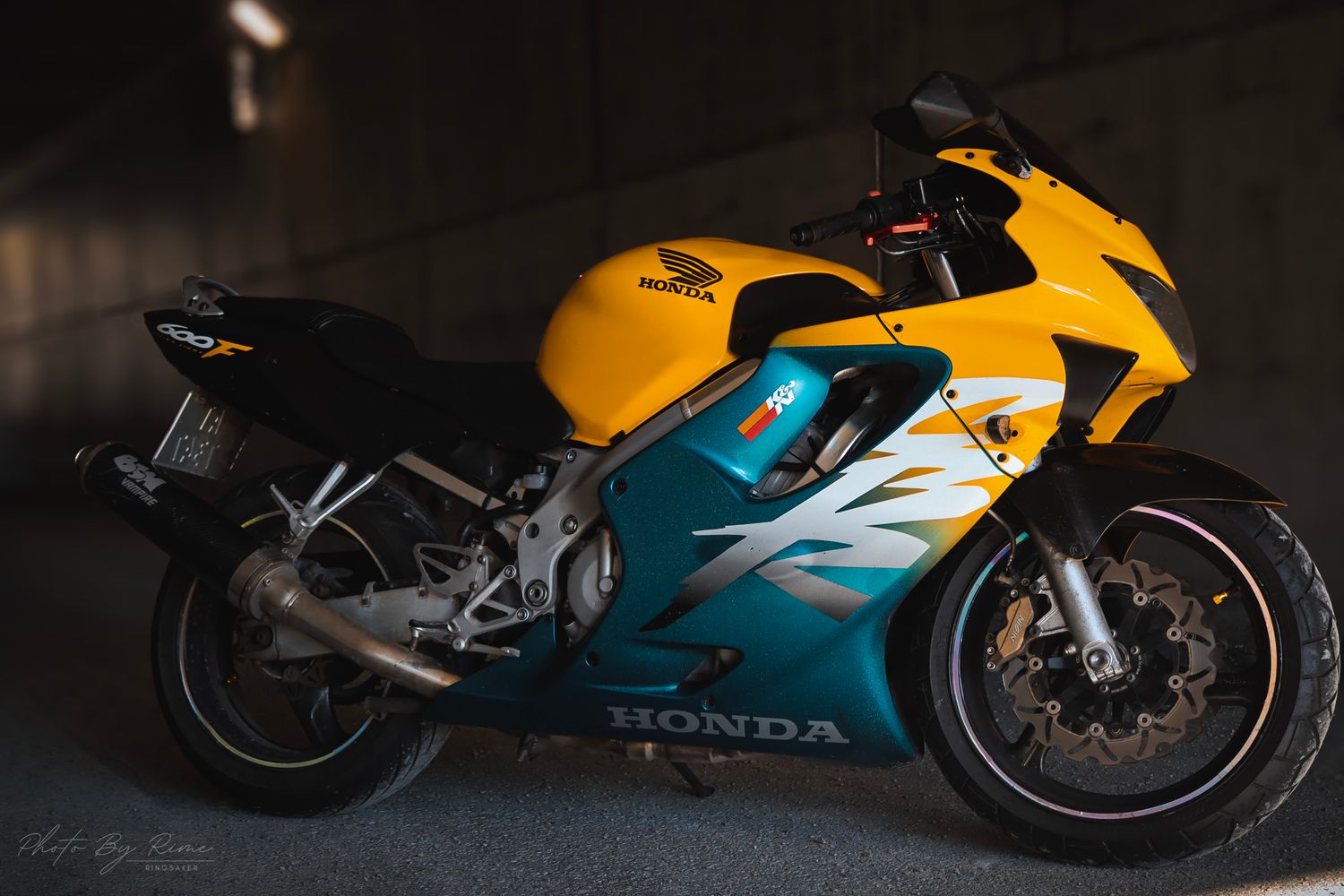 Gul og turkis Honda sportssykkel fotografert i en mørk garasje.