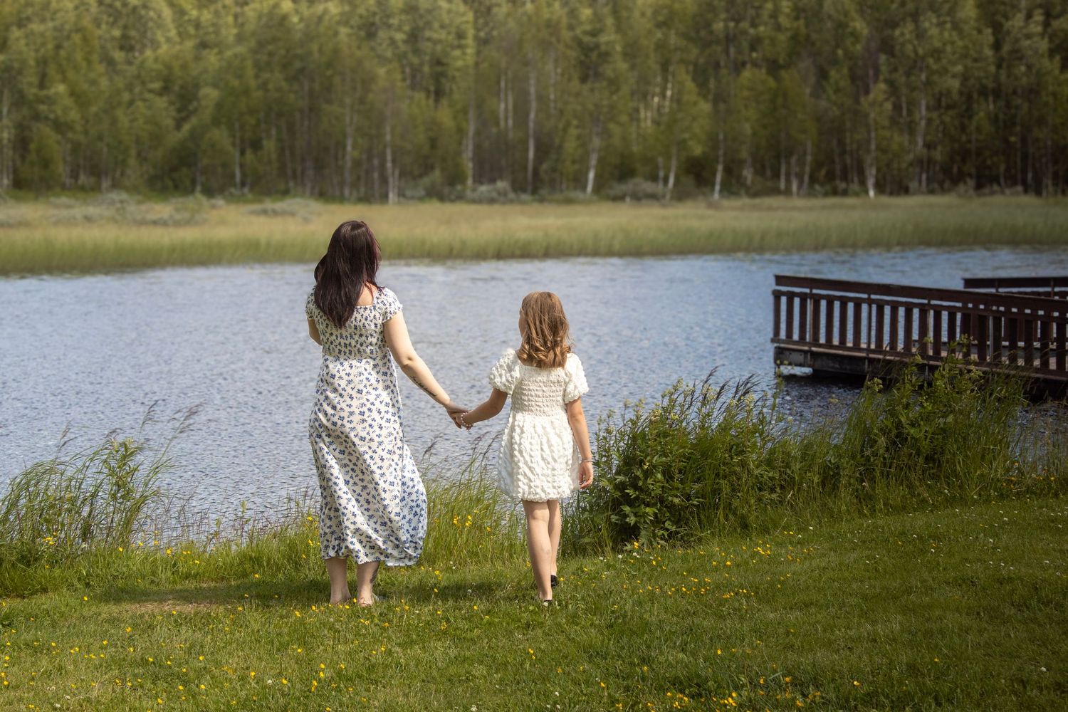 Mor og datter i sommerkjoler holder hender mens de går mot Næra.