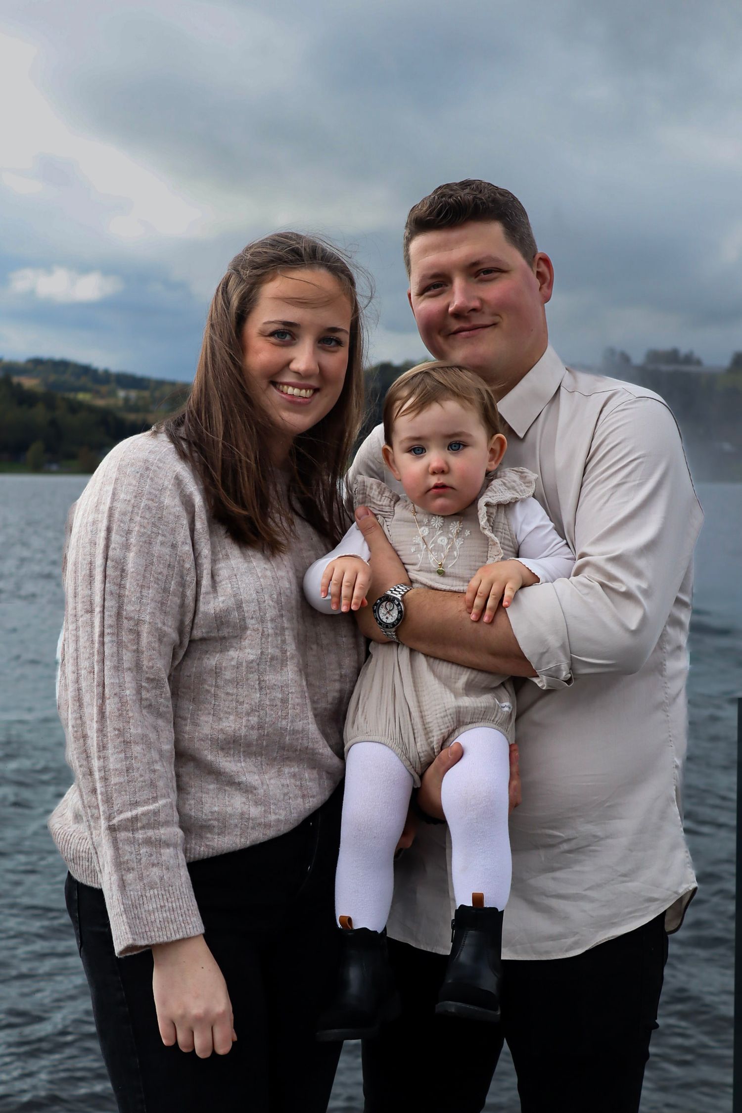 Familie med baby fotografert sammen ved Mjøsa på en overskyet dag.