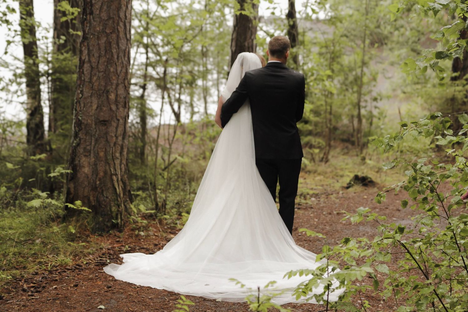 Brudepar fotografert bakfra sammen i en grønn skog.