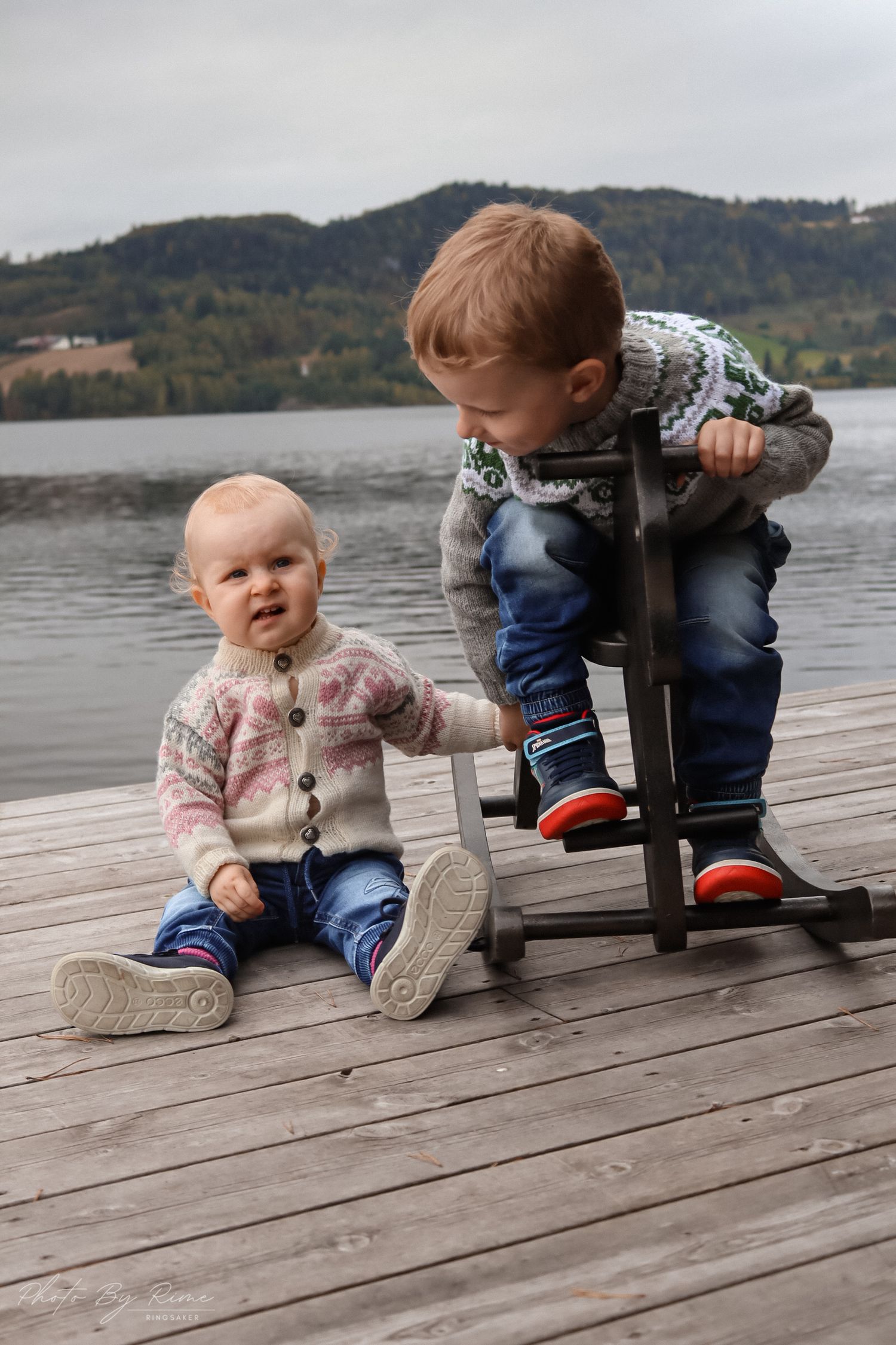 To søsken i strikkegensere fotografert på en trebrygge ved Mjøsa.