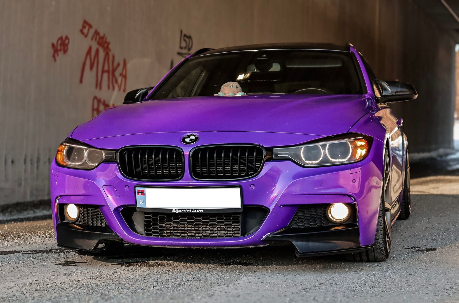 Lilla BMW 3-serie med svart grill fotografert ved en betongvegg.