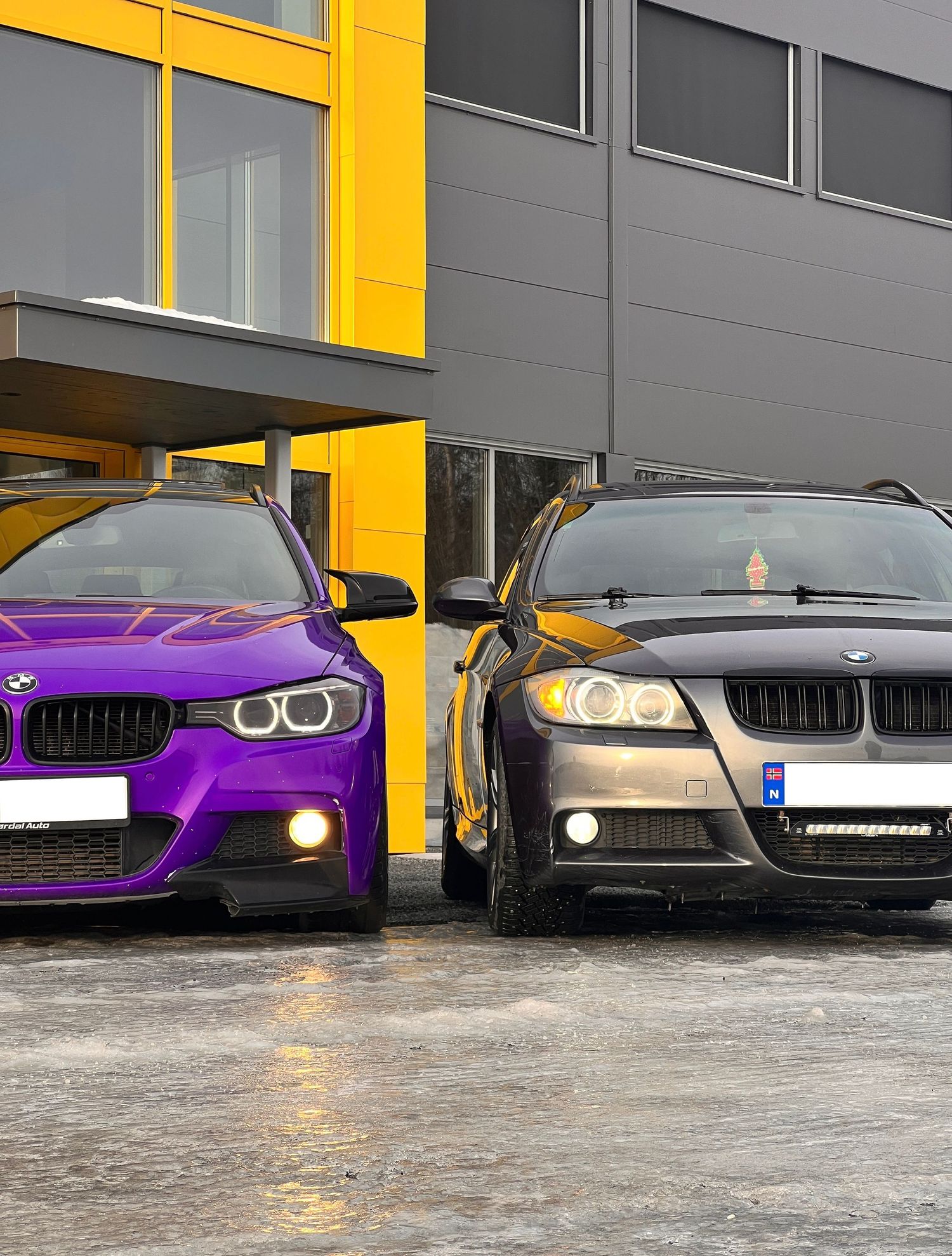 Lilla og mørkegrå BMW fotografert side om side foran en bygning med gule detaljer.
