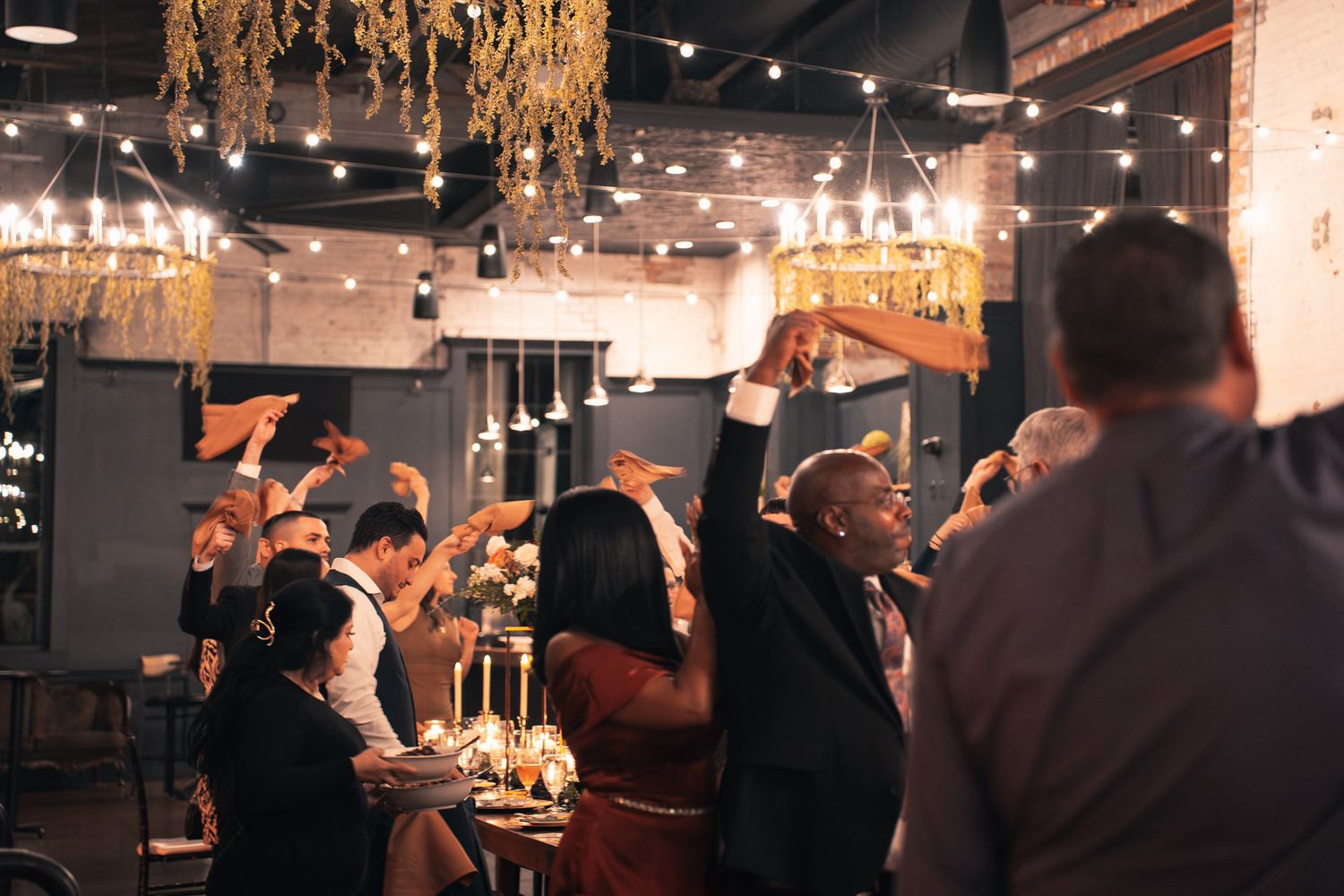 Dimly lit jazz club interior with string lights and exposed brick walls showing multiple tables of patrons enjoying live music.