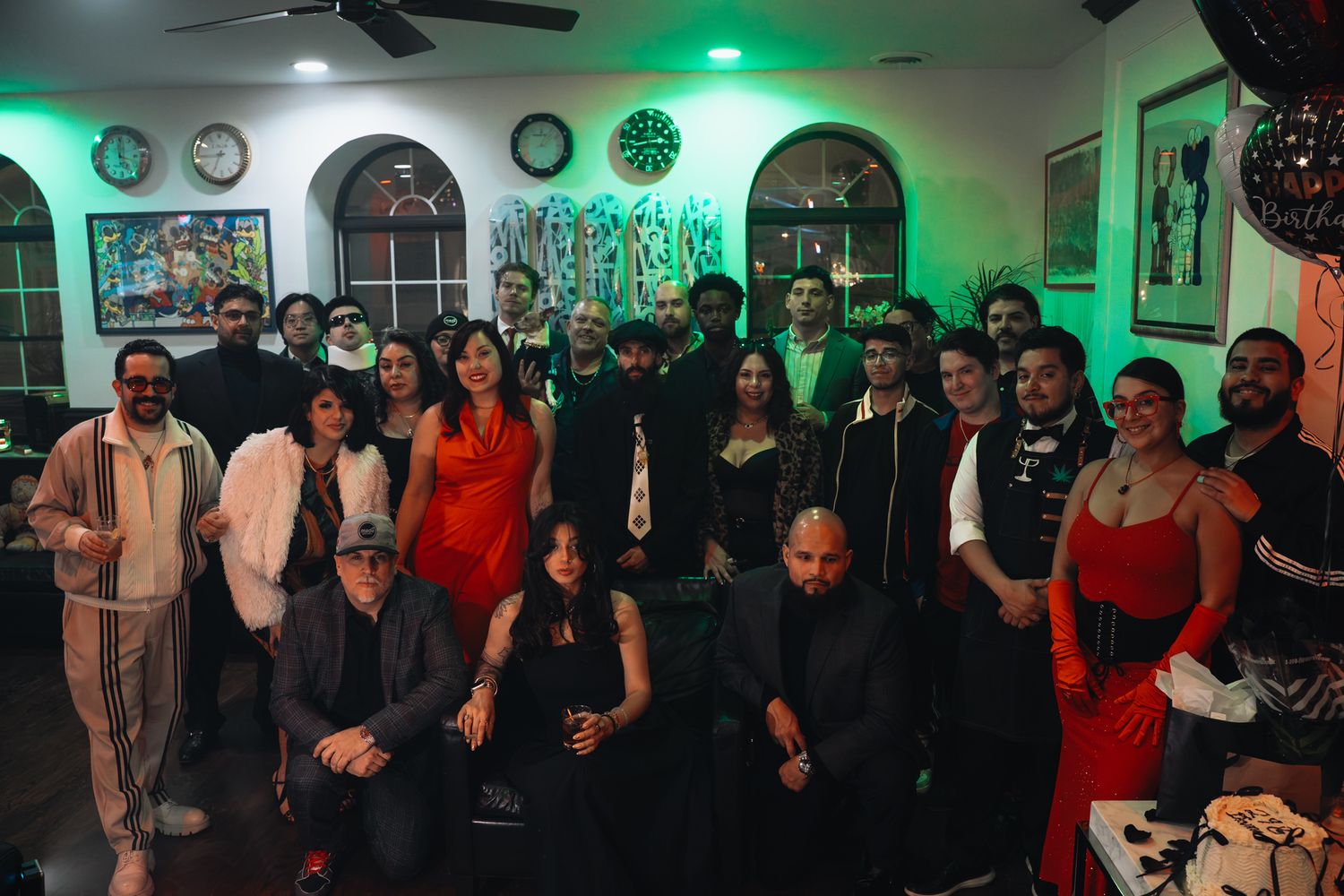 Large group of party guests pose together in a room with green lighting and wall decorations.