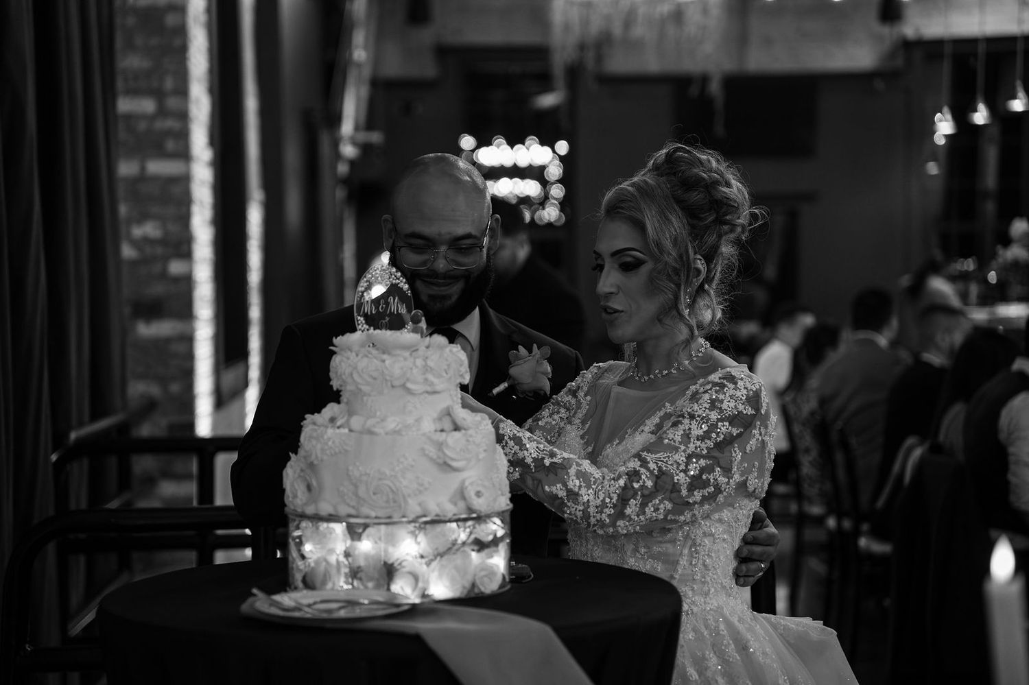 A black and white wedding reception scene shows guests dancing and celebrating in an elegant venue.