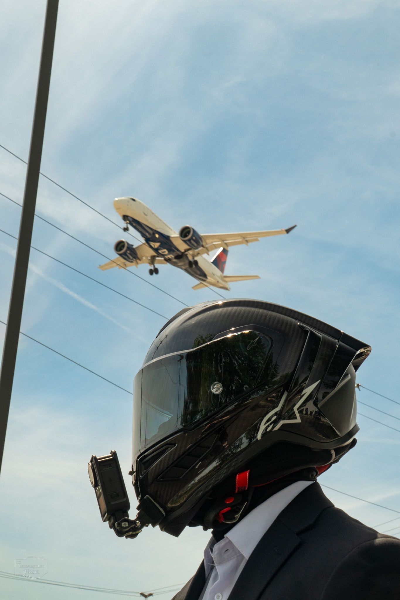 Black motorcycle helmet silhouetted against blue sky with airplane flying overhead.