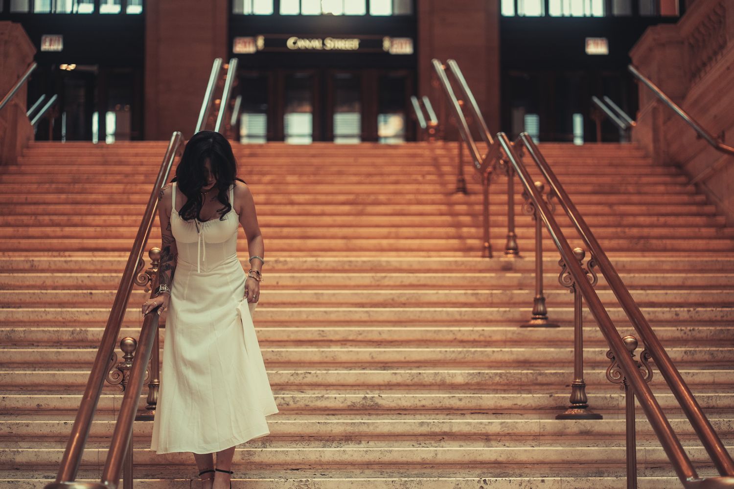 A person in a light yellow dress walks up red brick stairs with metal railings in an urban setting.