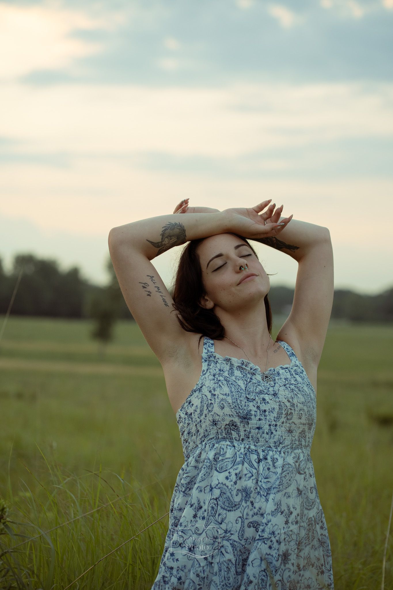 A person in a floral dress stretches in a sunlit meadow against a blue sky.