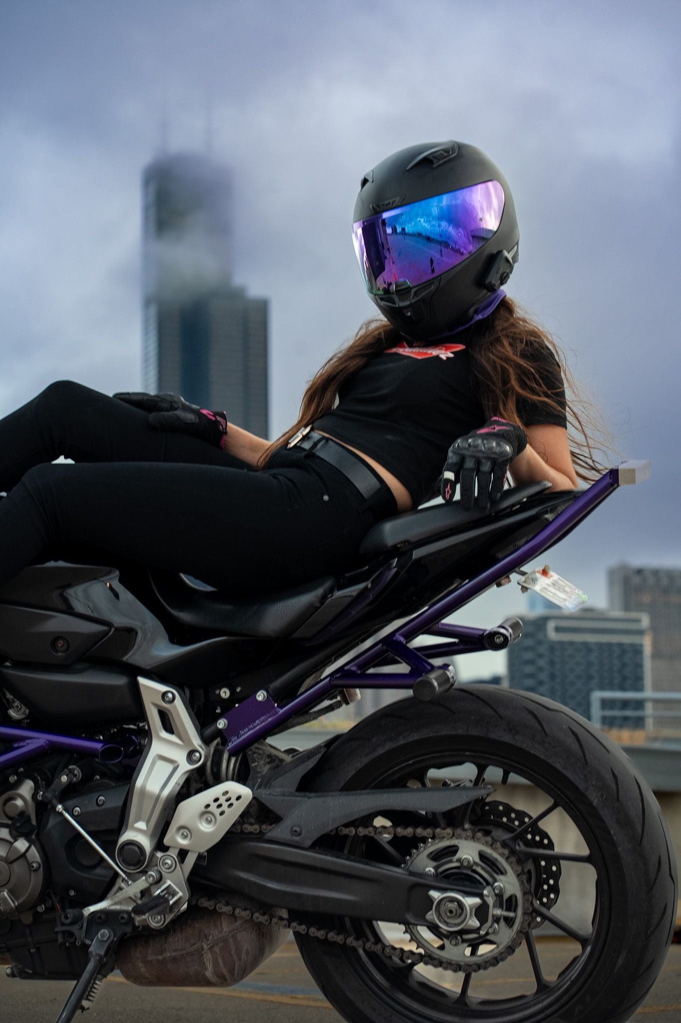 A black and purple sportbike with rider photographed from a low angle against city buildings.