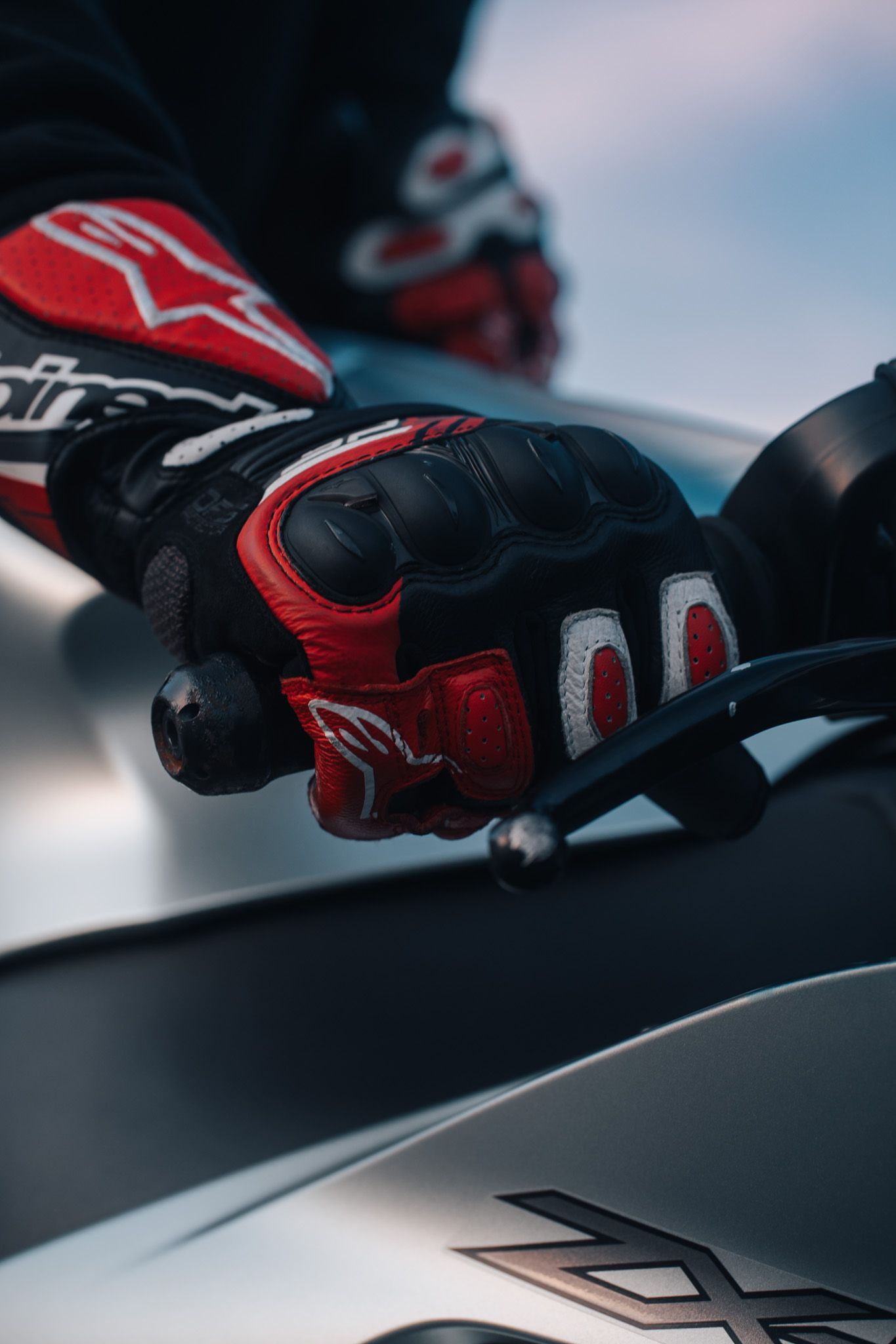 Close-up of red and black motorcycle gloves resting on a bike's tank.