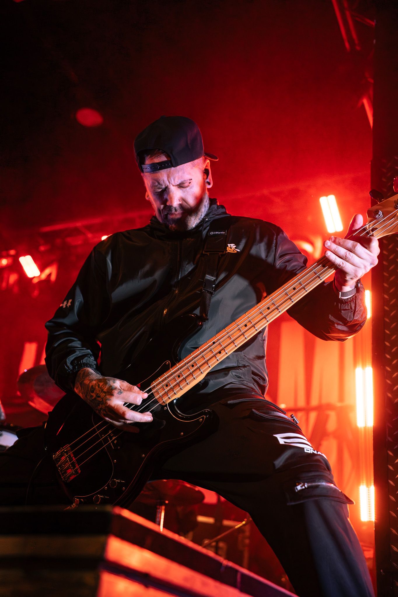 Bass guitarist performing on stage with dramatic red lighting effects.