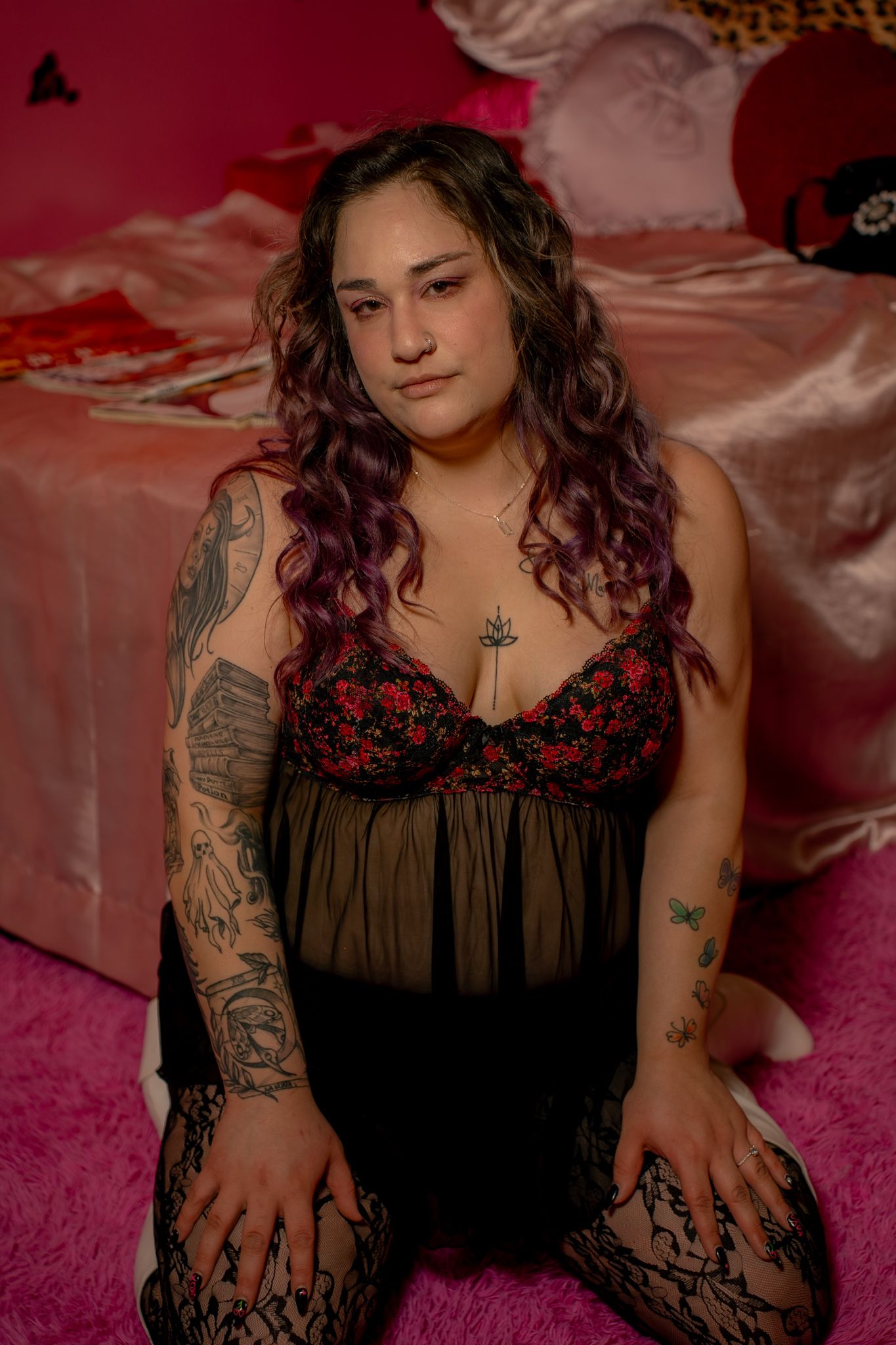 A person wearing a black lace lingerie top poses on pink bedding in a boudoir photoshoot.