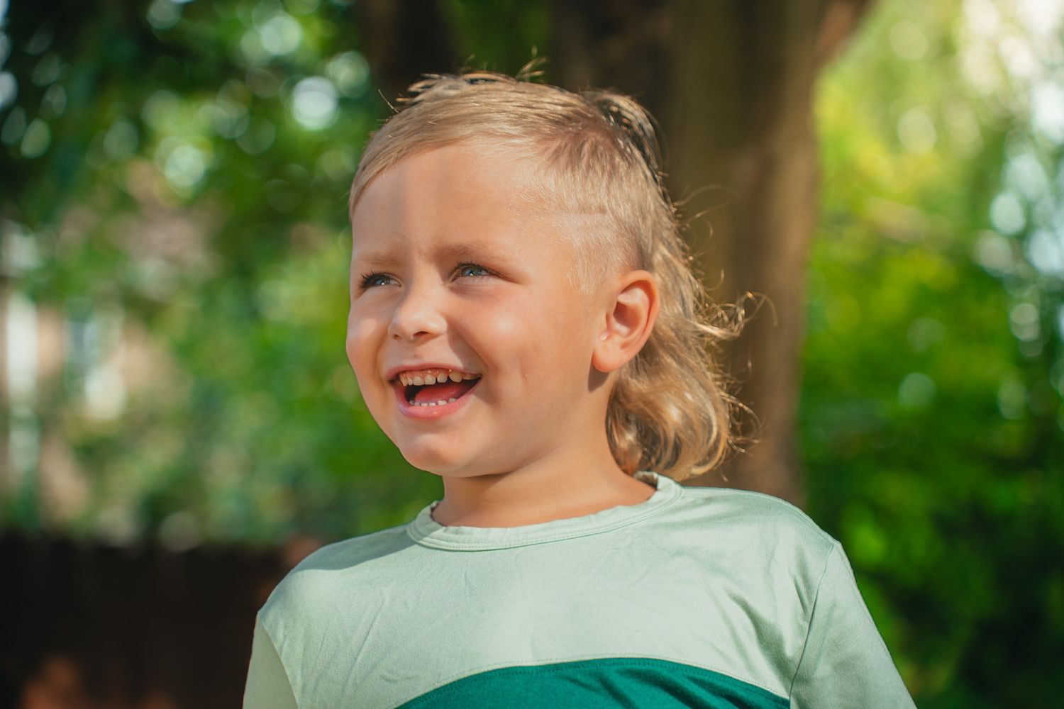 A laughing child in light green clothing plays in a sunny outdoor setting.