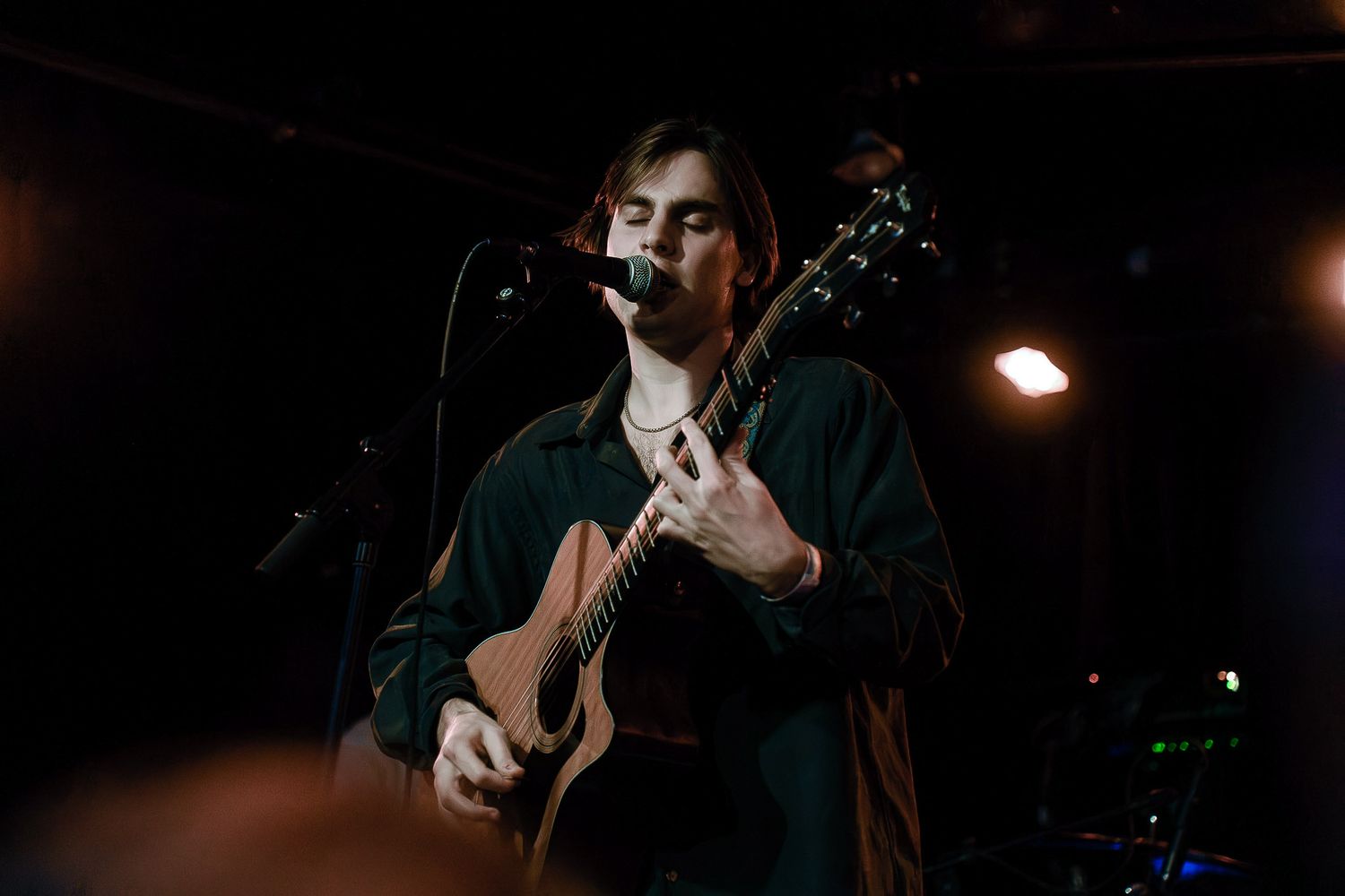 Dark concert stage with musicians performing on guitars in dramatic lighting.