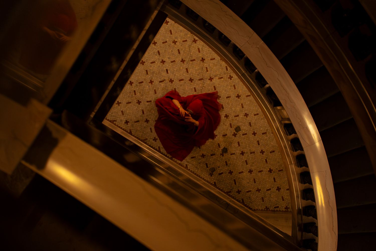 Person in red dress photographed from above on ornate spiral staircase in dramatic warm lighting.