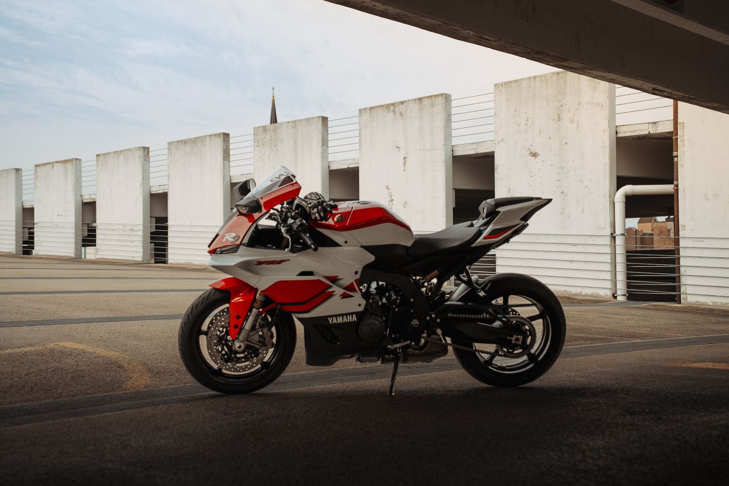 Red and white sport motorcycle parked in front of concrete structure at dusk.