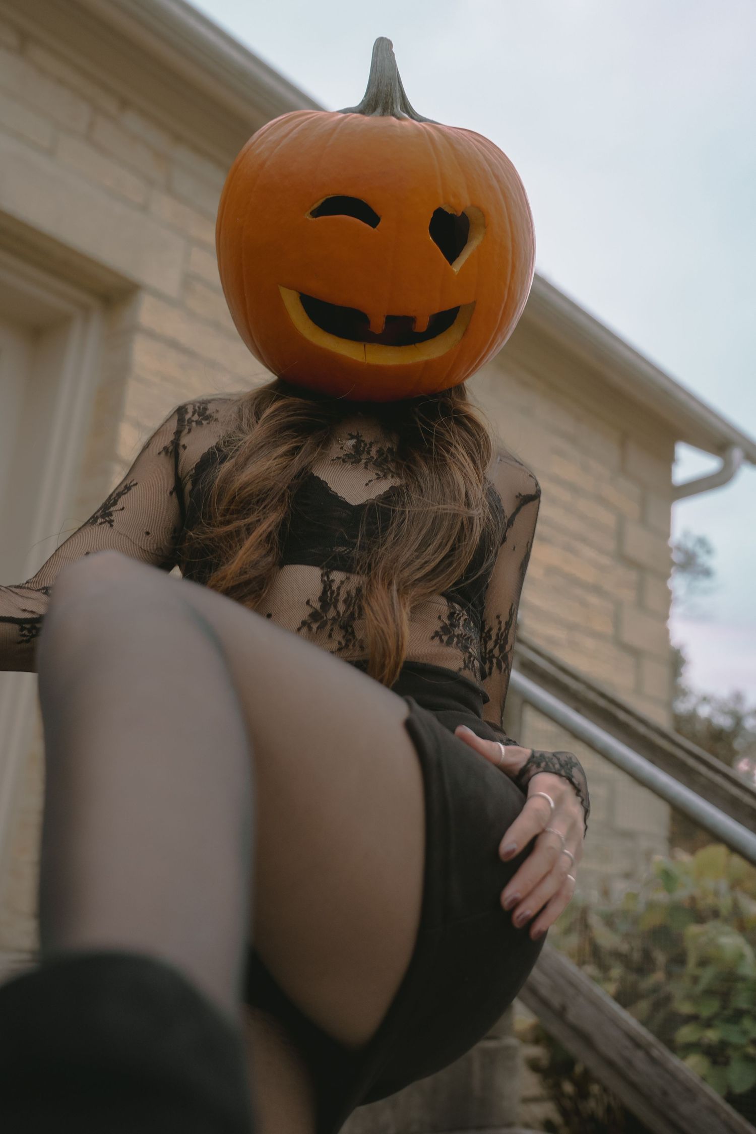 A spooky Halloween figure with a pumpkin head poses against a light-colored building exterior.
