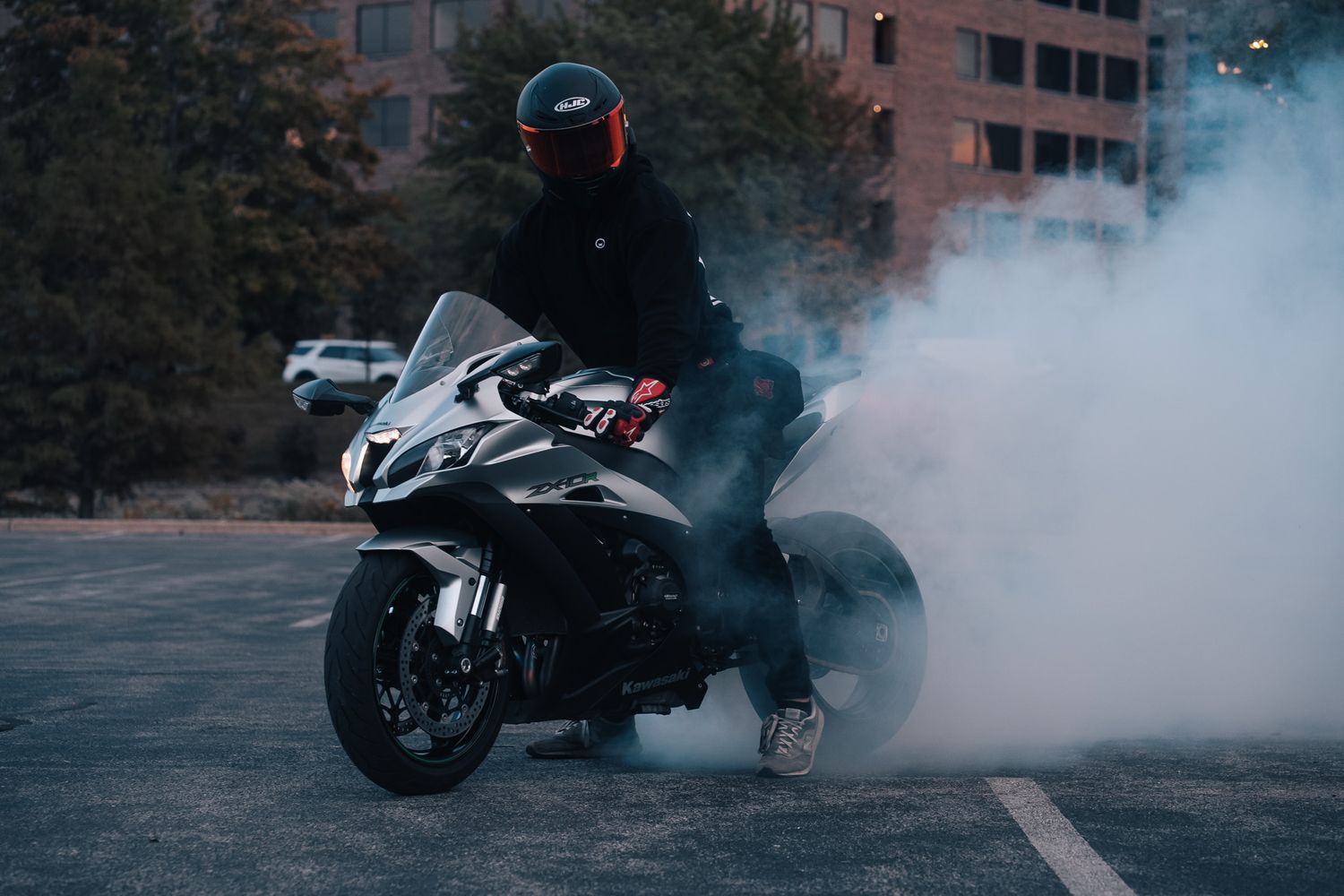 Motorcycle performing a burnout with smoke in a parking lot.