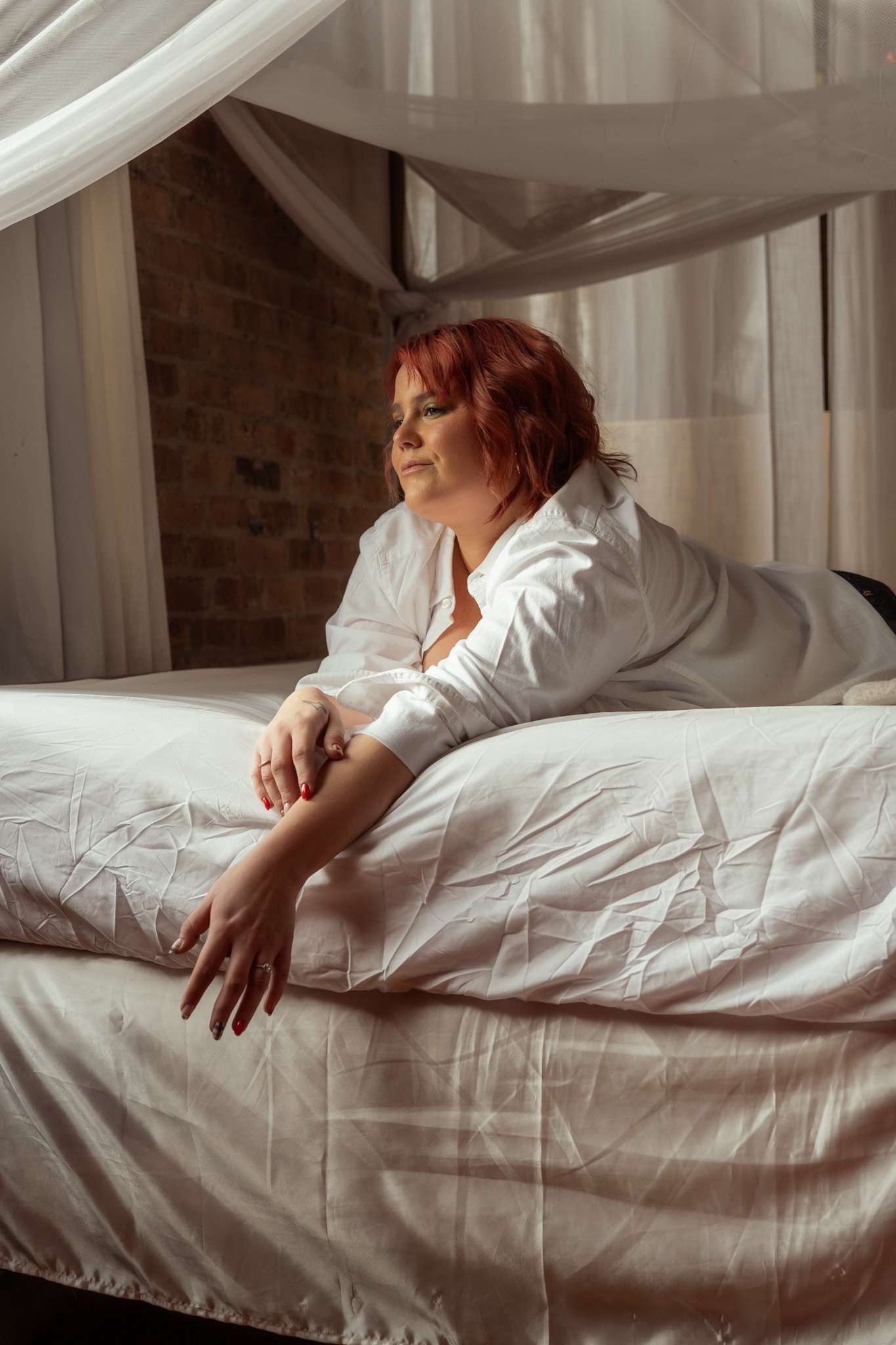 A figure rests on white bedding in soft natural light streaming through sheer curtains.