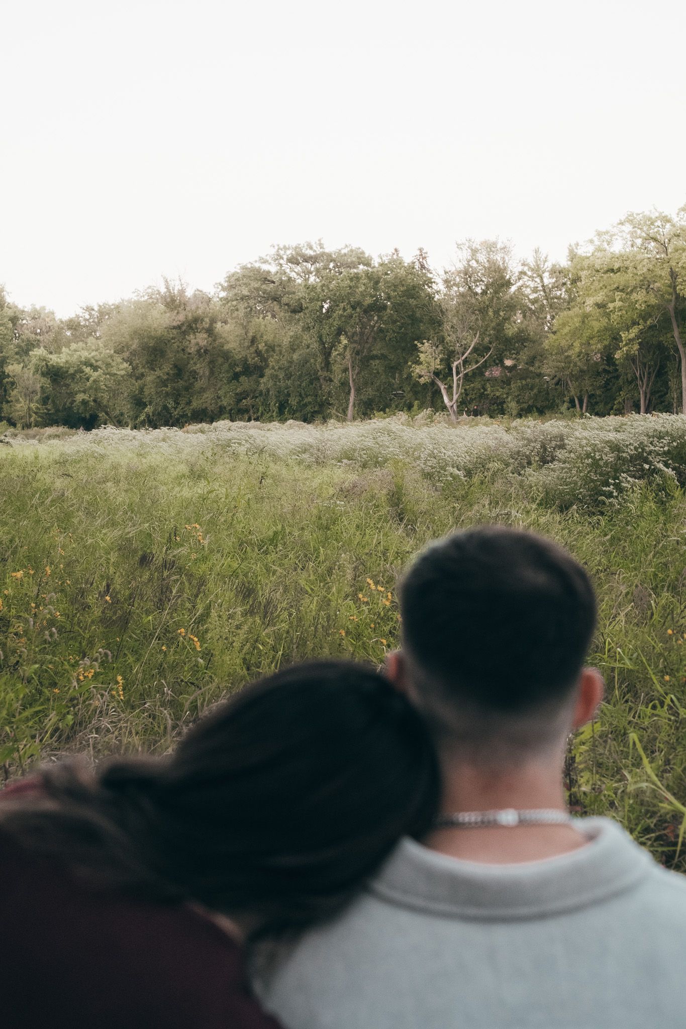 Couple sitting together in a serene outdoor field with tall grass and trees in the background.