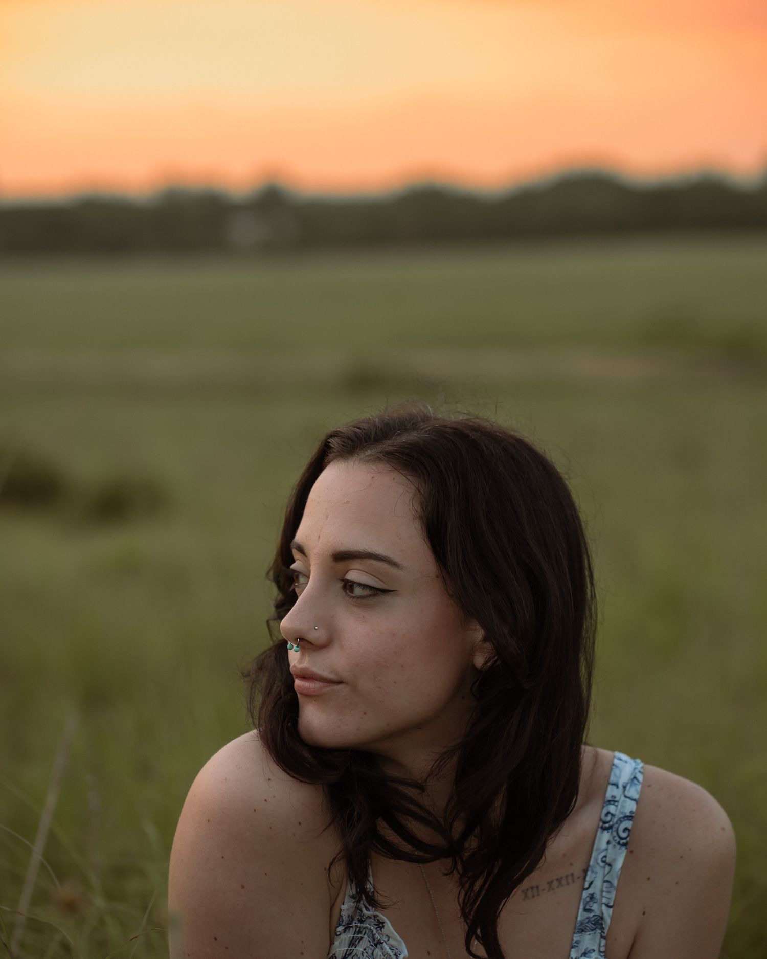 Artistic portrait of someone in a floral top against a warm sunset sky.