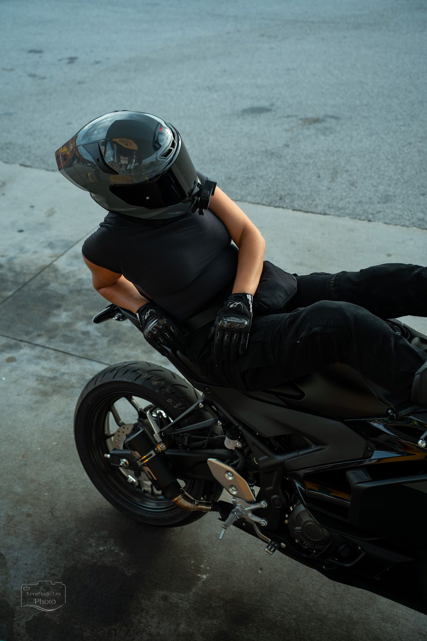 Motorcycle rider in black gear performs low-angle maneuver on dark pavement.