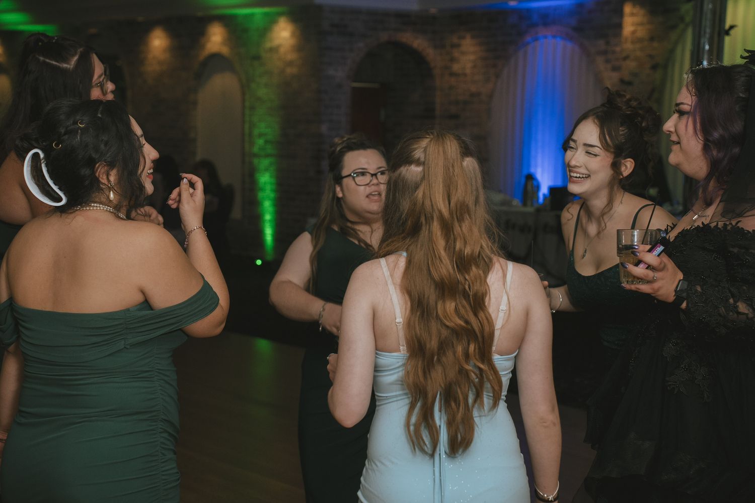 Party guests dance and socialize at an evening event with colorful green and blue lighting.