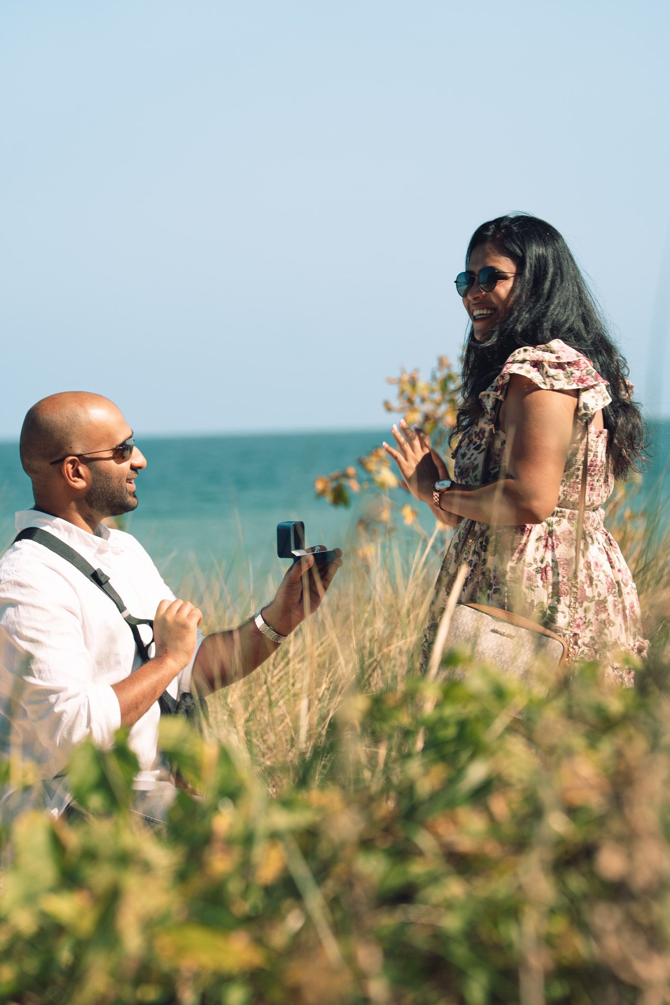 Photographers taking pictures in tall grass near turquoise ocean waters.