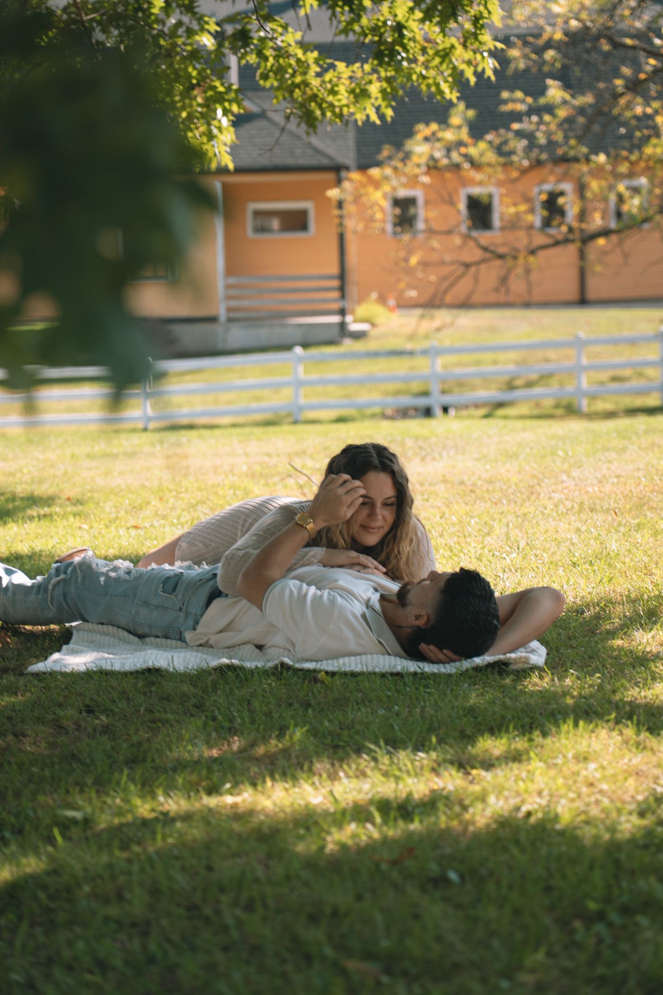 A romantic couple relaxes on blankets in a sun-dappled field.