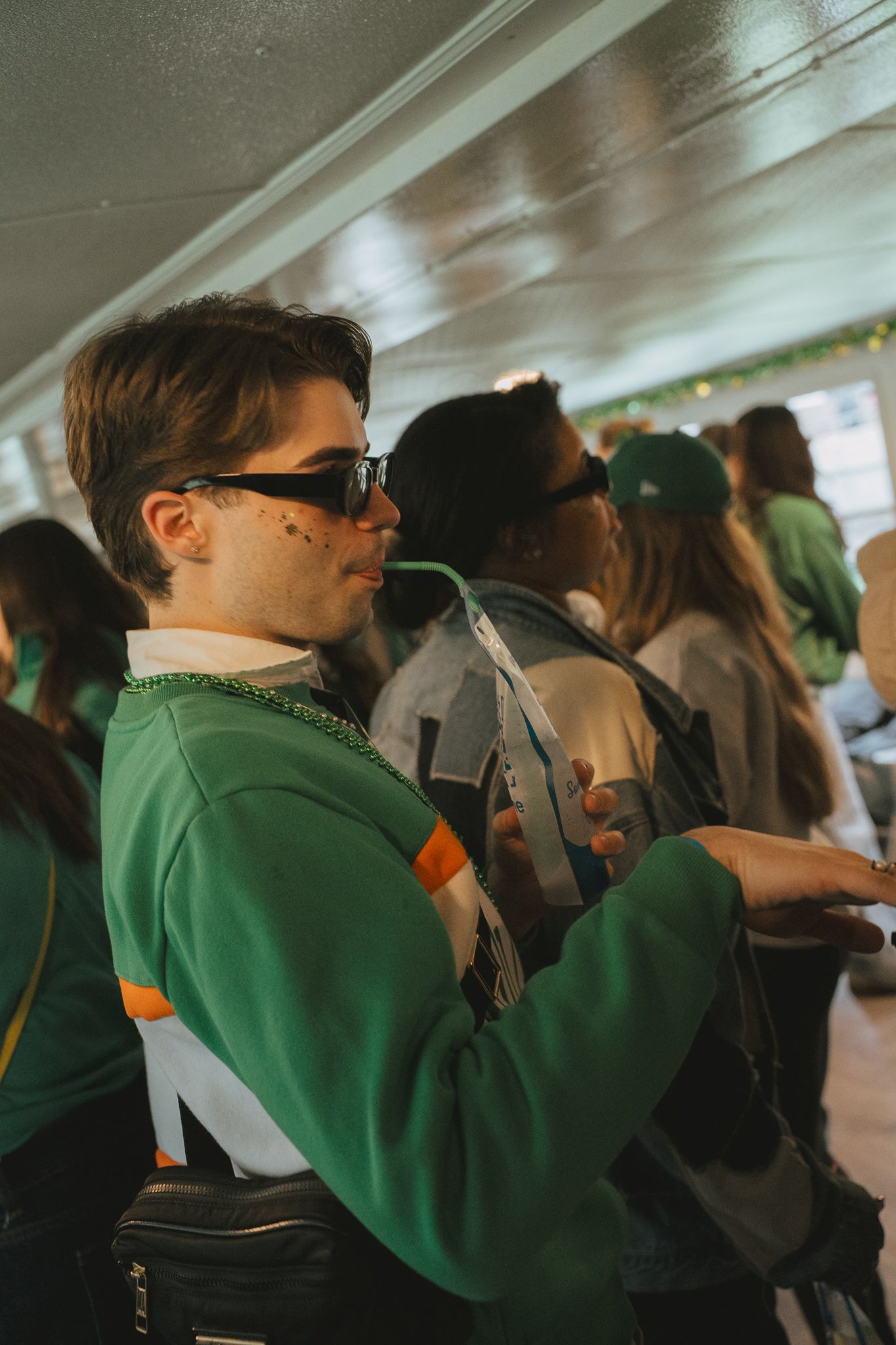 Students in green uniforms stand together in a crowded indoor space looking in the same direction.