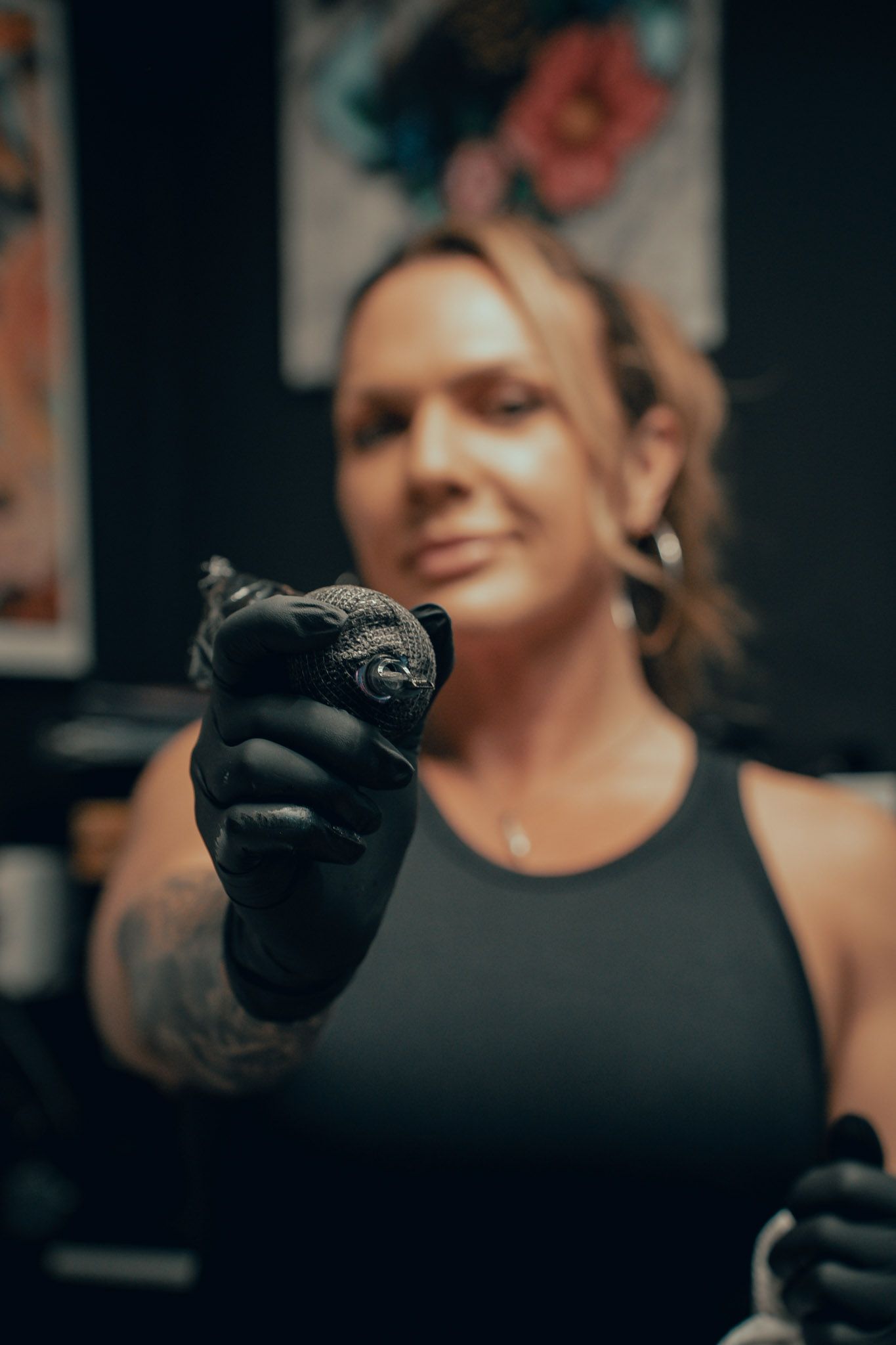 A tattoo artist in black gloves holds up a tattoo machine in a professional tattoo studio.