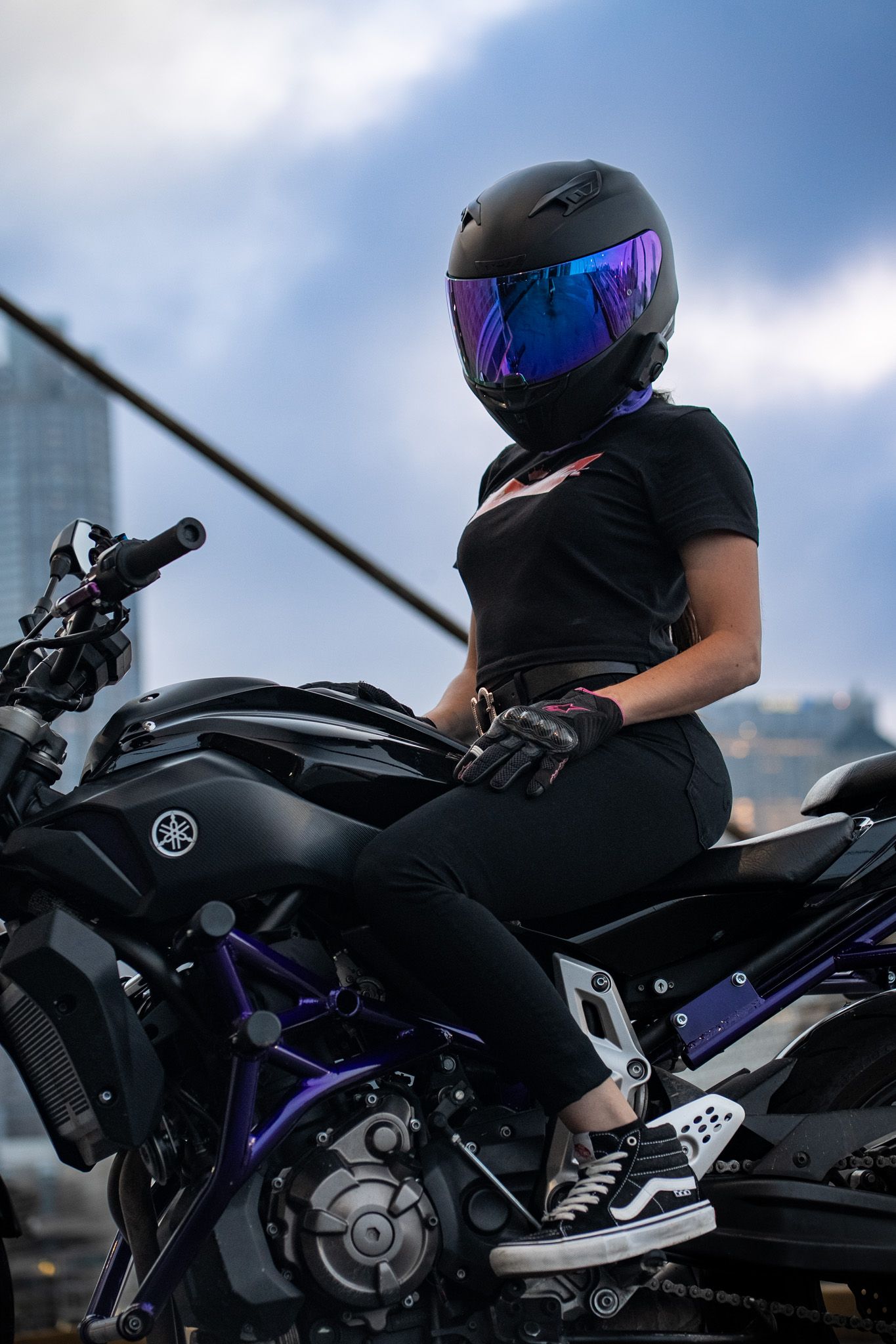 Black motorcycle with purple accents against urban backdrop with rider in matching gear.