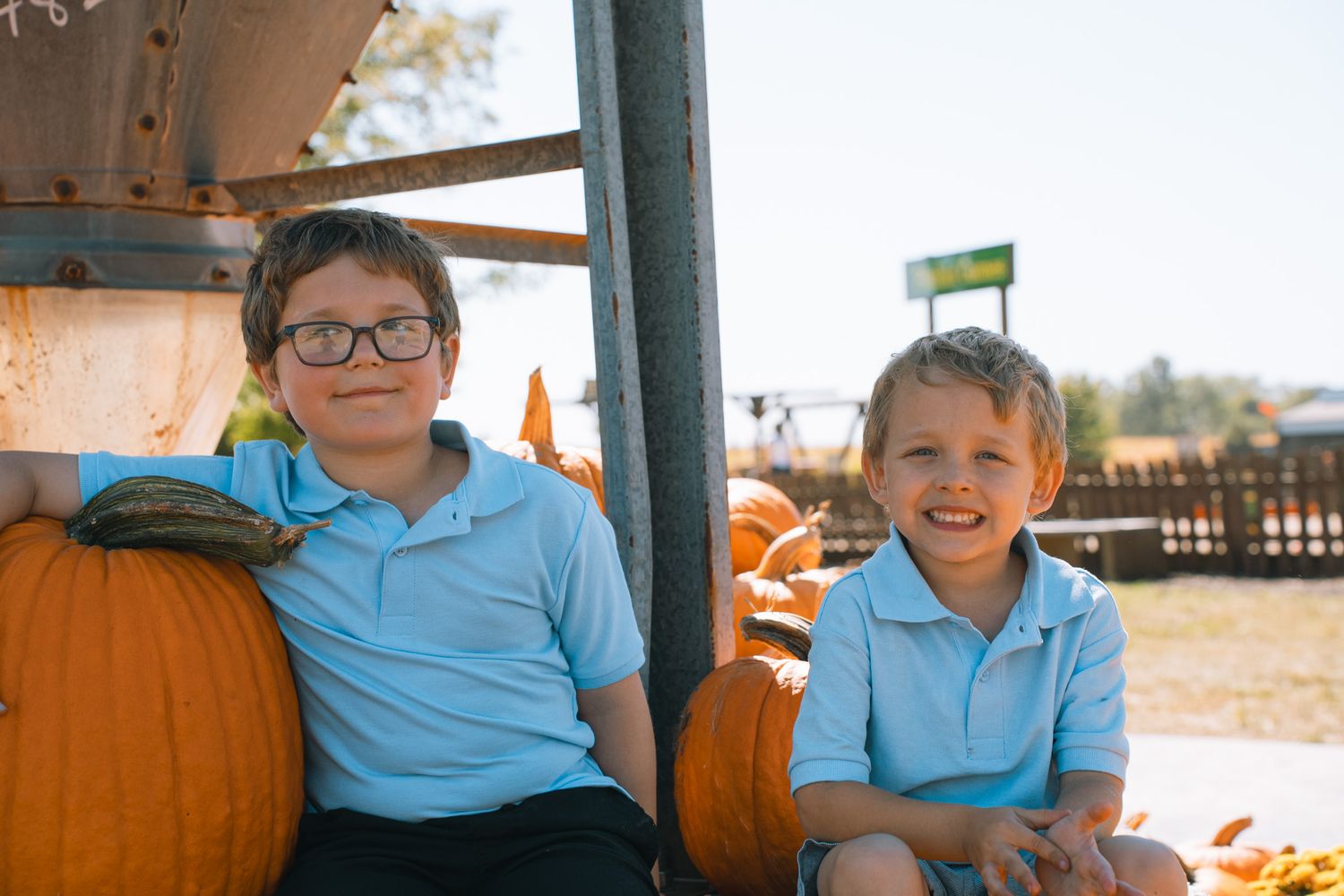 Children in light blue shirts smiling and enjoying time at a pumpkin patch during fall.