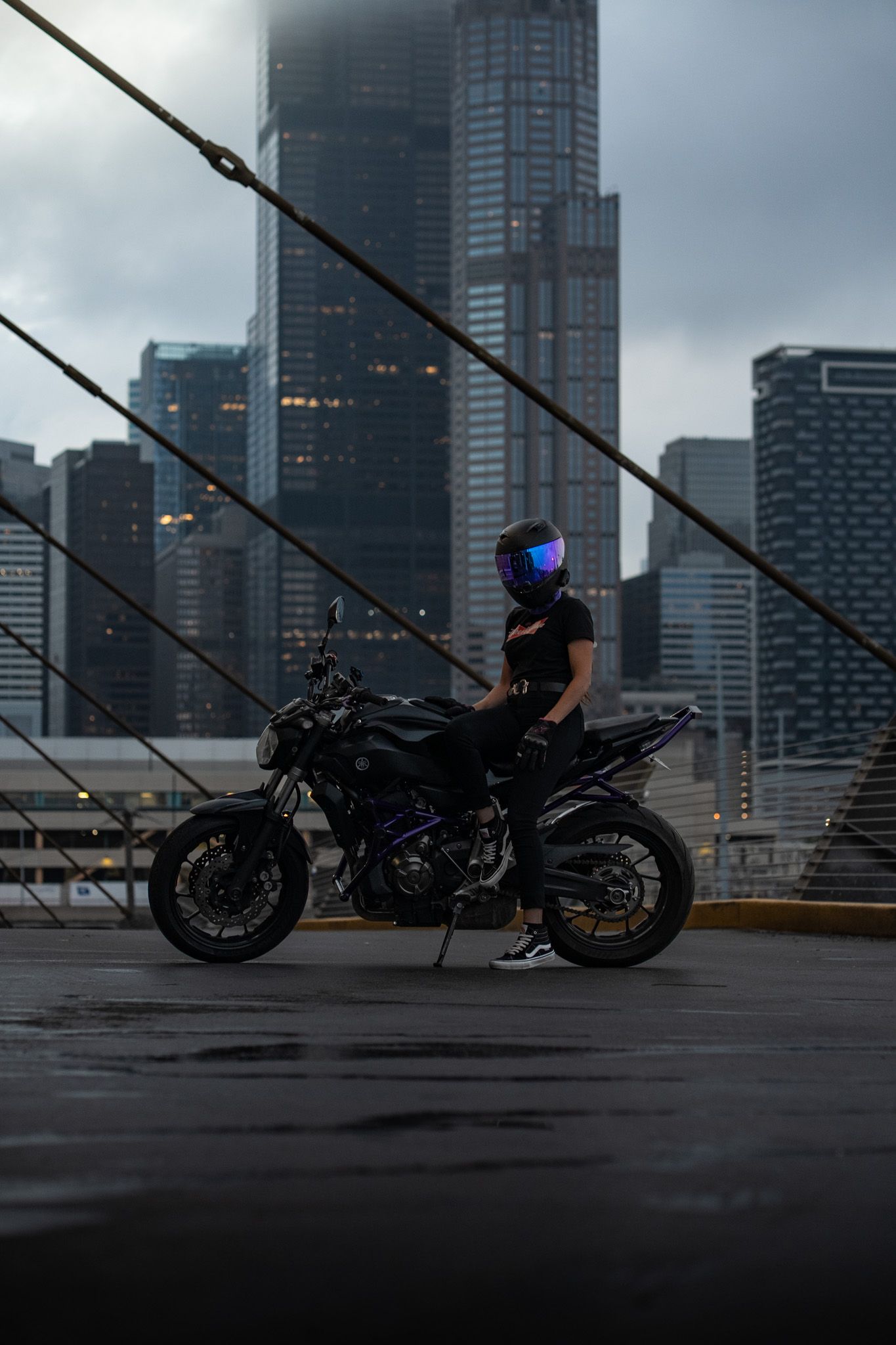 Motorcycles staged on bridge with dramatic cityscape and diagonal support cables visible.