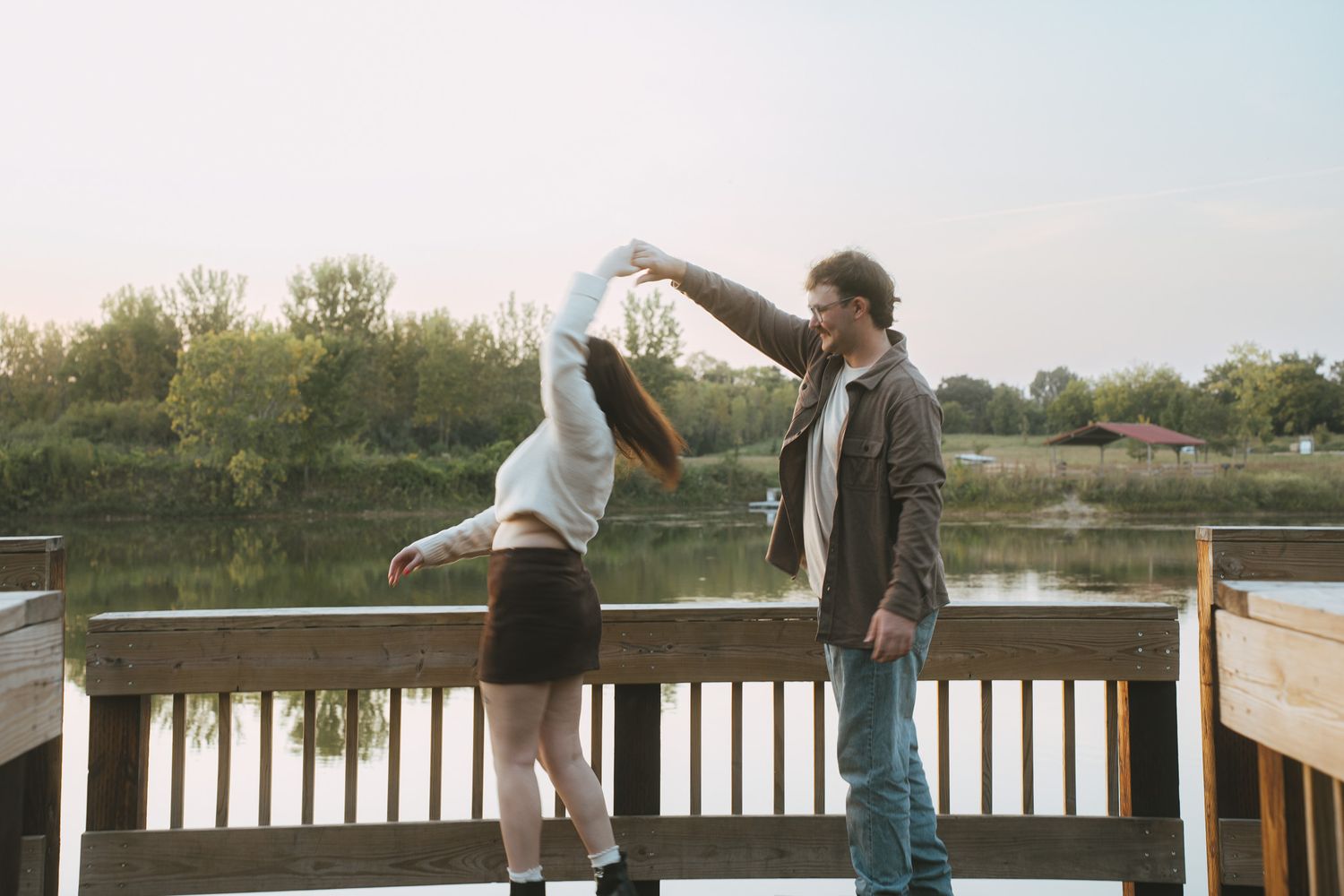 People playfully balance on wooden railings by a lake during sunset.