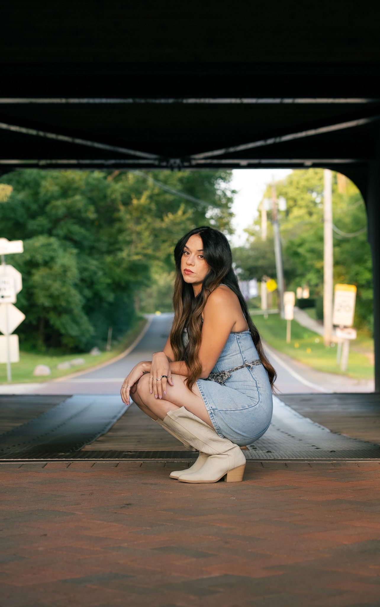 A person in casual denim sits on a brick path with trees in the background.