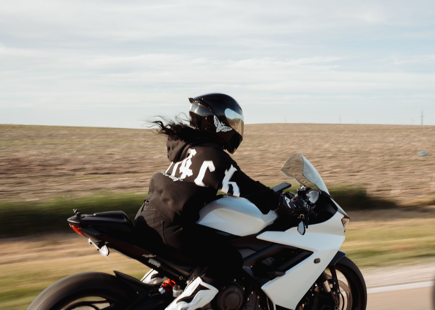 Motorcyclist in black jacket and helmet riding a white sport bike on an open road at high speed.