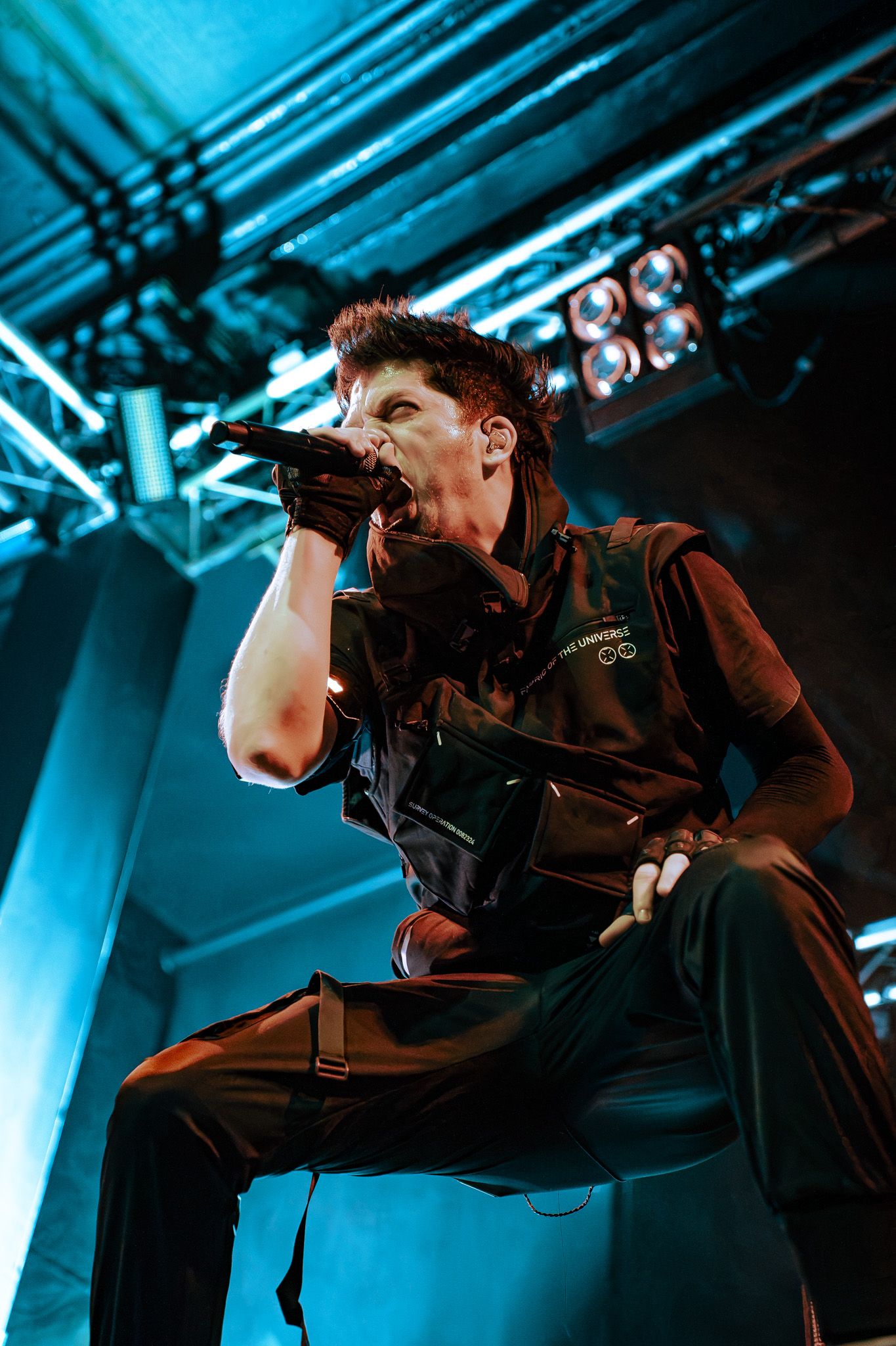 Performer in black clothing singing on stage with blue theatrical lighting.